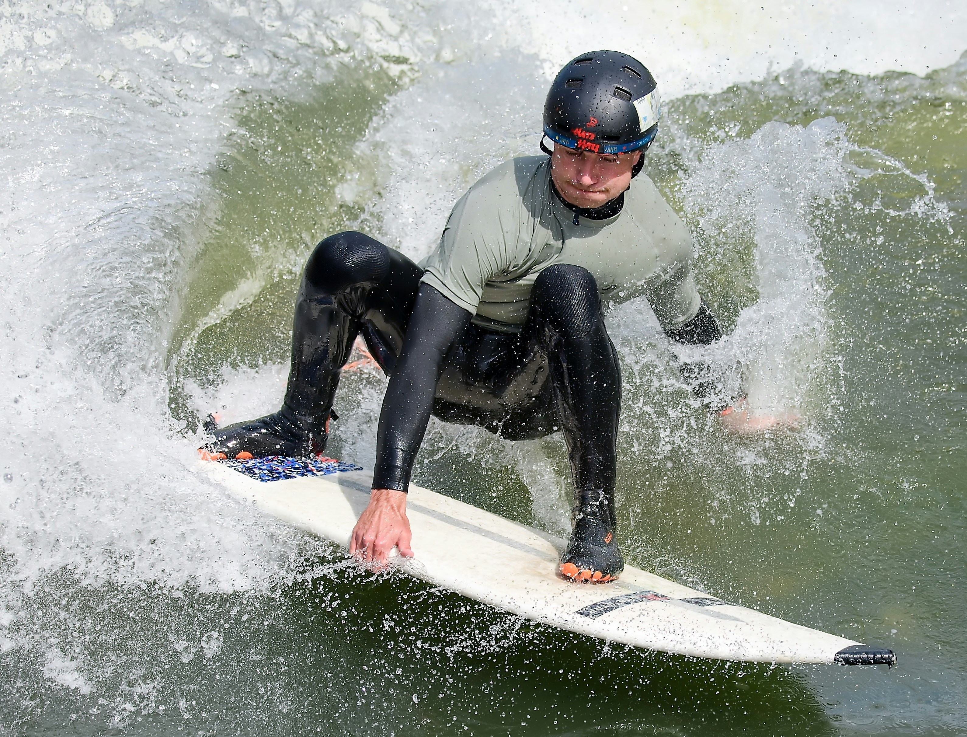 Um homem de roupa de neoprene e capacete surfa uma onda.