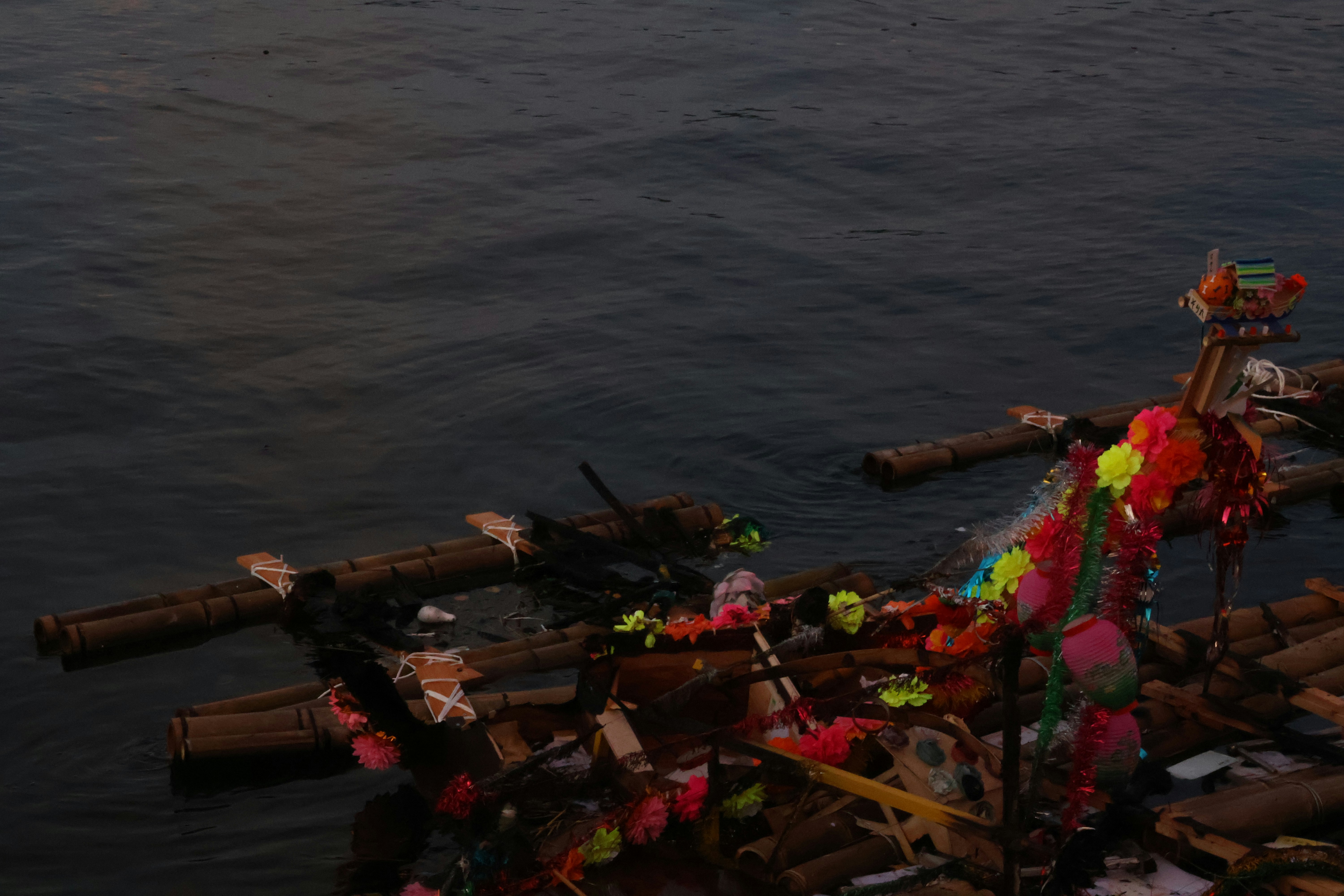 Colorful ribbons decorate a log raft floating on dark water.