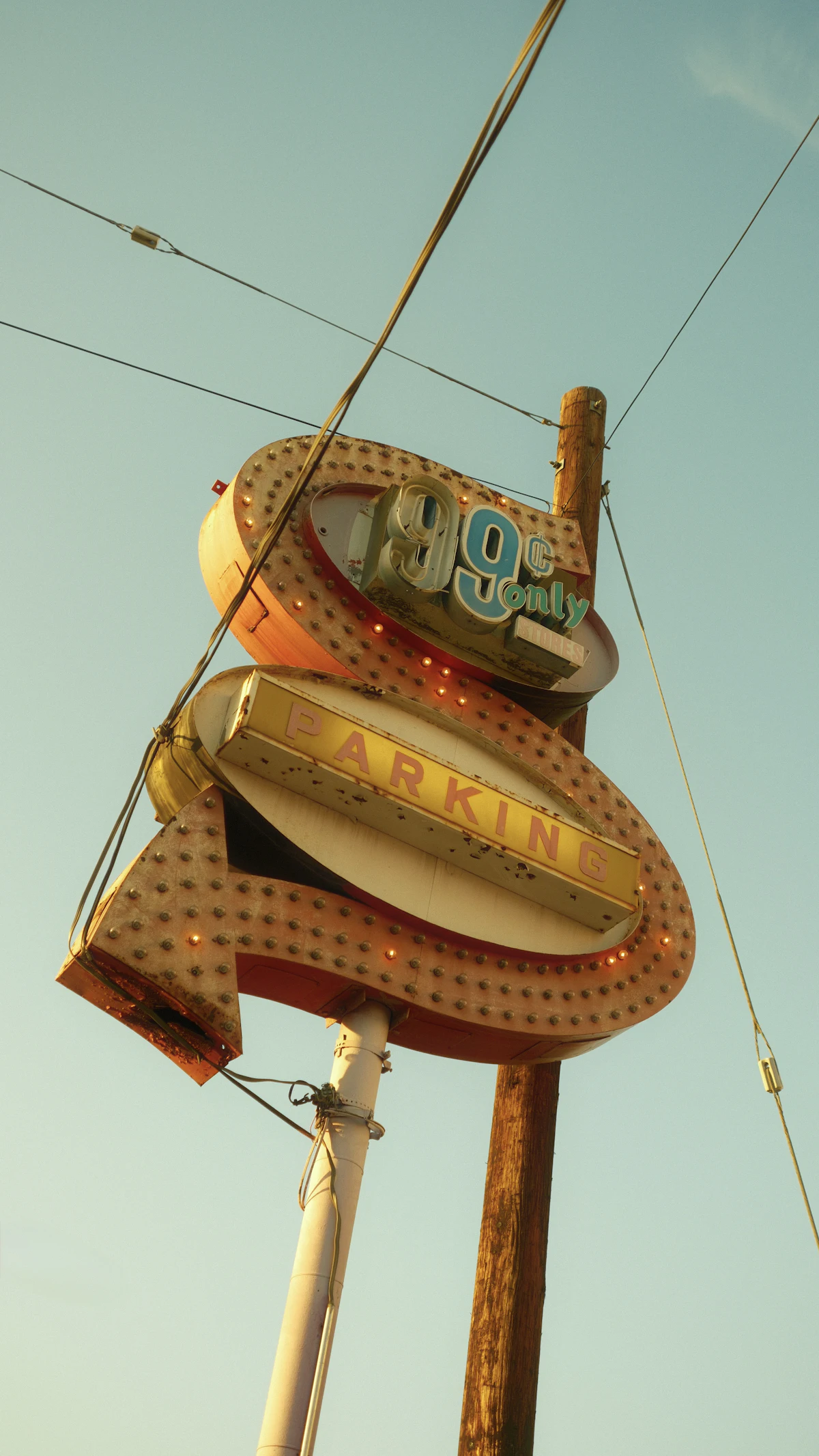 A weathered vintage neon sign on a pole against a pale sky, its bulbs and lettering rusted and worn.