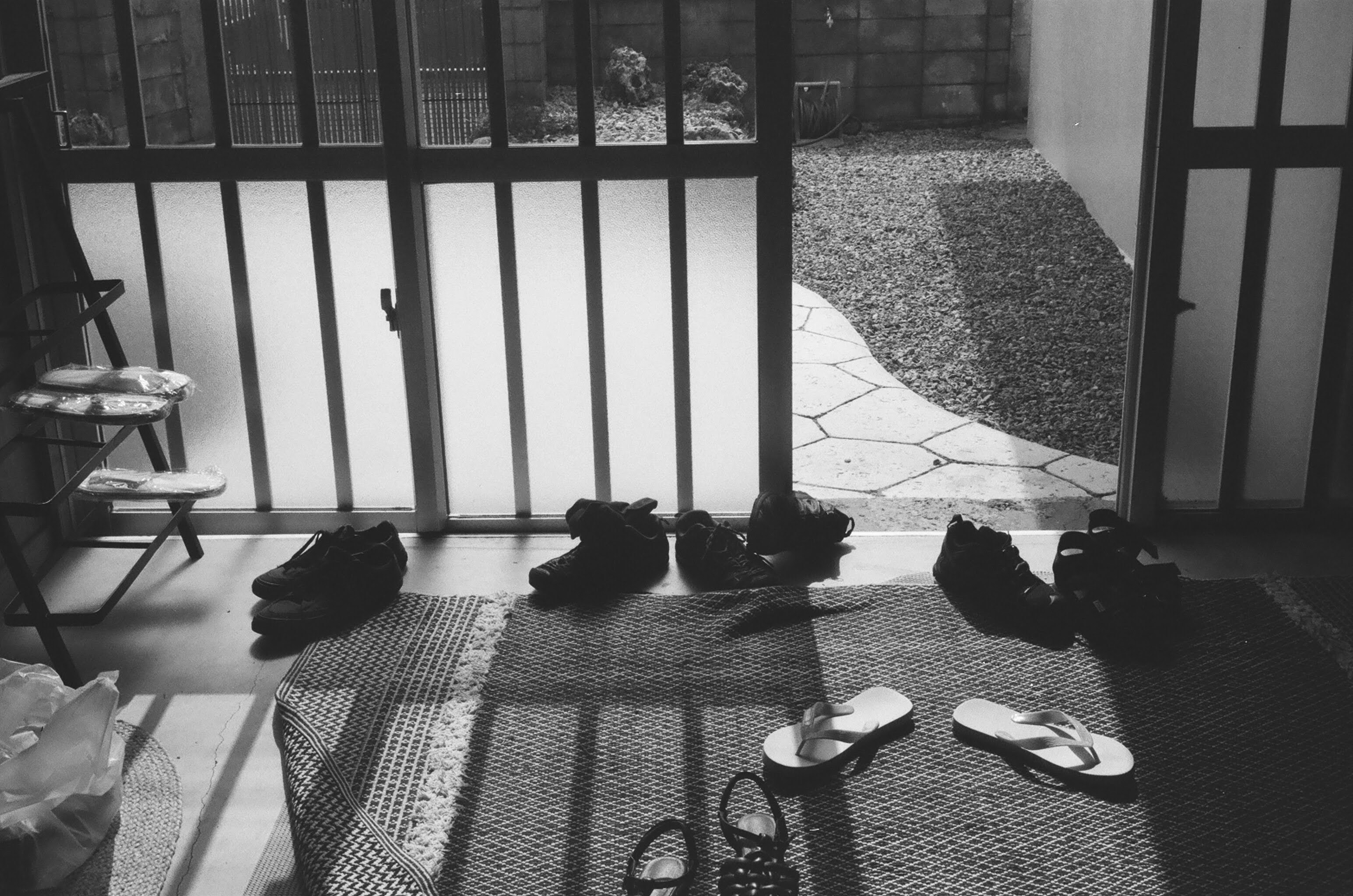 Chaussures disposées sur un tapis près d’une porte de jardin ensoleillée.