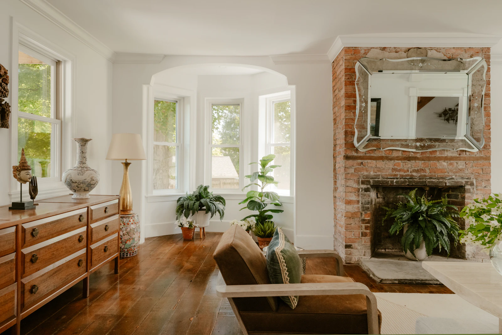 Brown upholstered armchair in a traditional living room with wood floors, a lamp, and a brick fireplace.