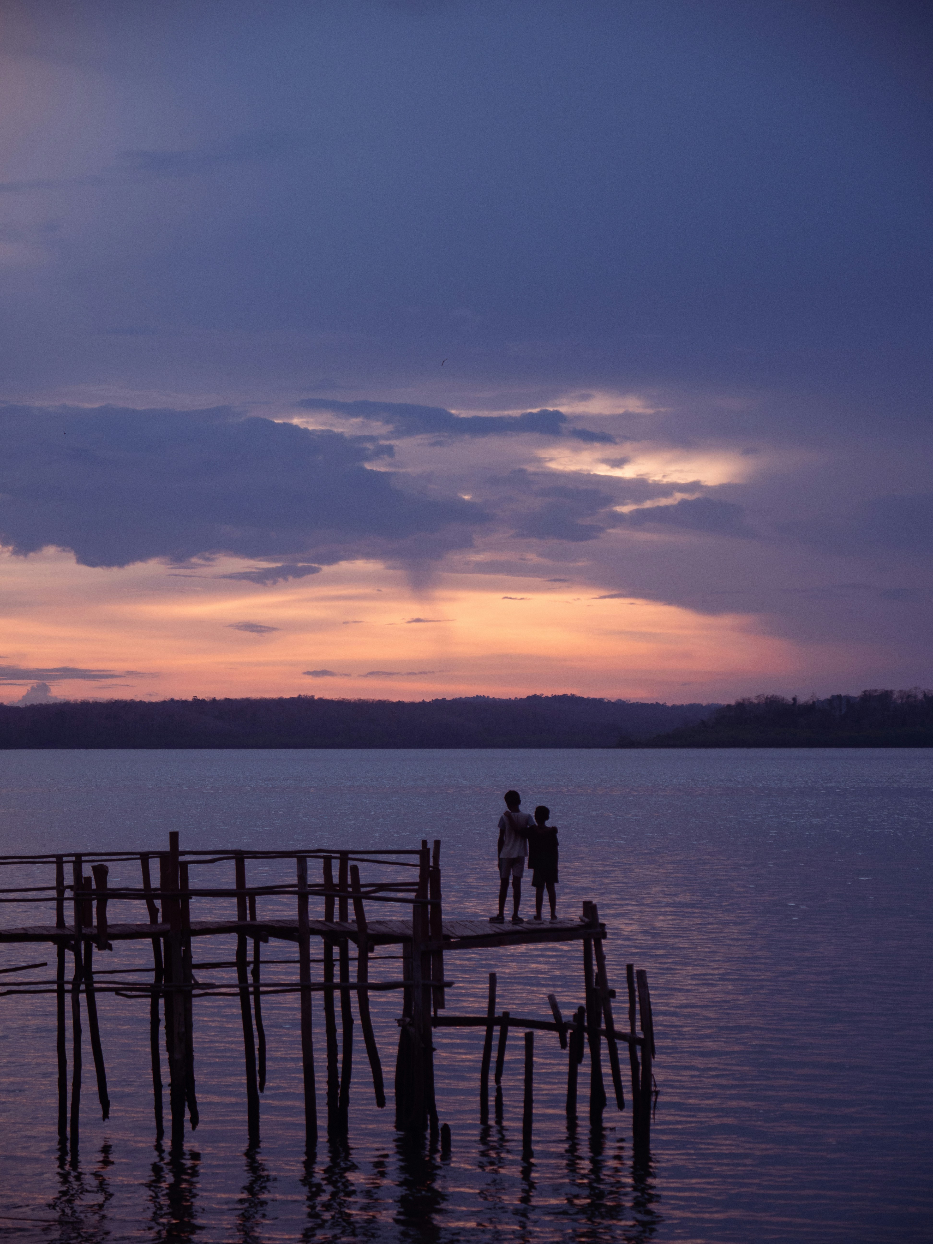 Silhouetted figures on a pier watching a colorful sunset
