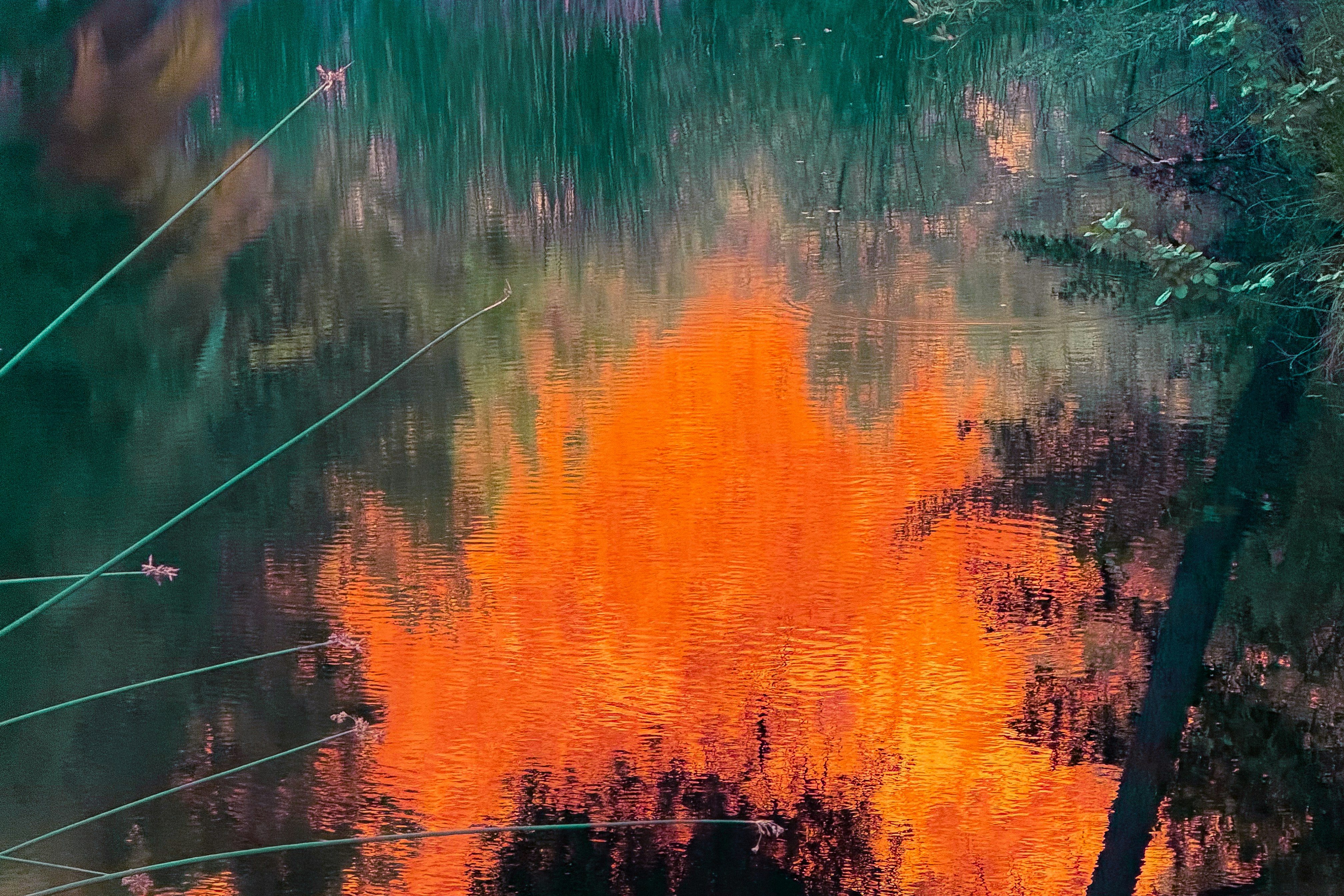 Orange and green reflections on rippling water with visible lines.