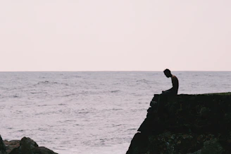 A person sits on a cliff overlooking the ocean.
