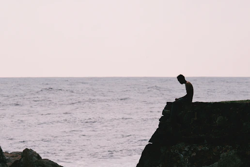 A person sits on a cliff overlooking the ocean.