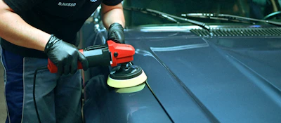 Person polishing a blue car's hood with an orbital buffer.
