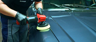 Person polishing a blue car's hood with an orbital buffer.