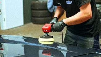 A person polishes a dark car with an electric polisher.