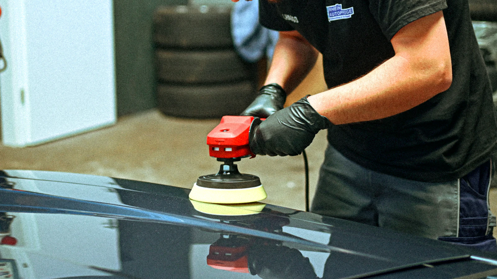 Technician machine-polishing a dark car during paint correction