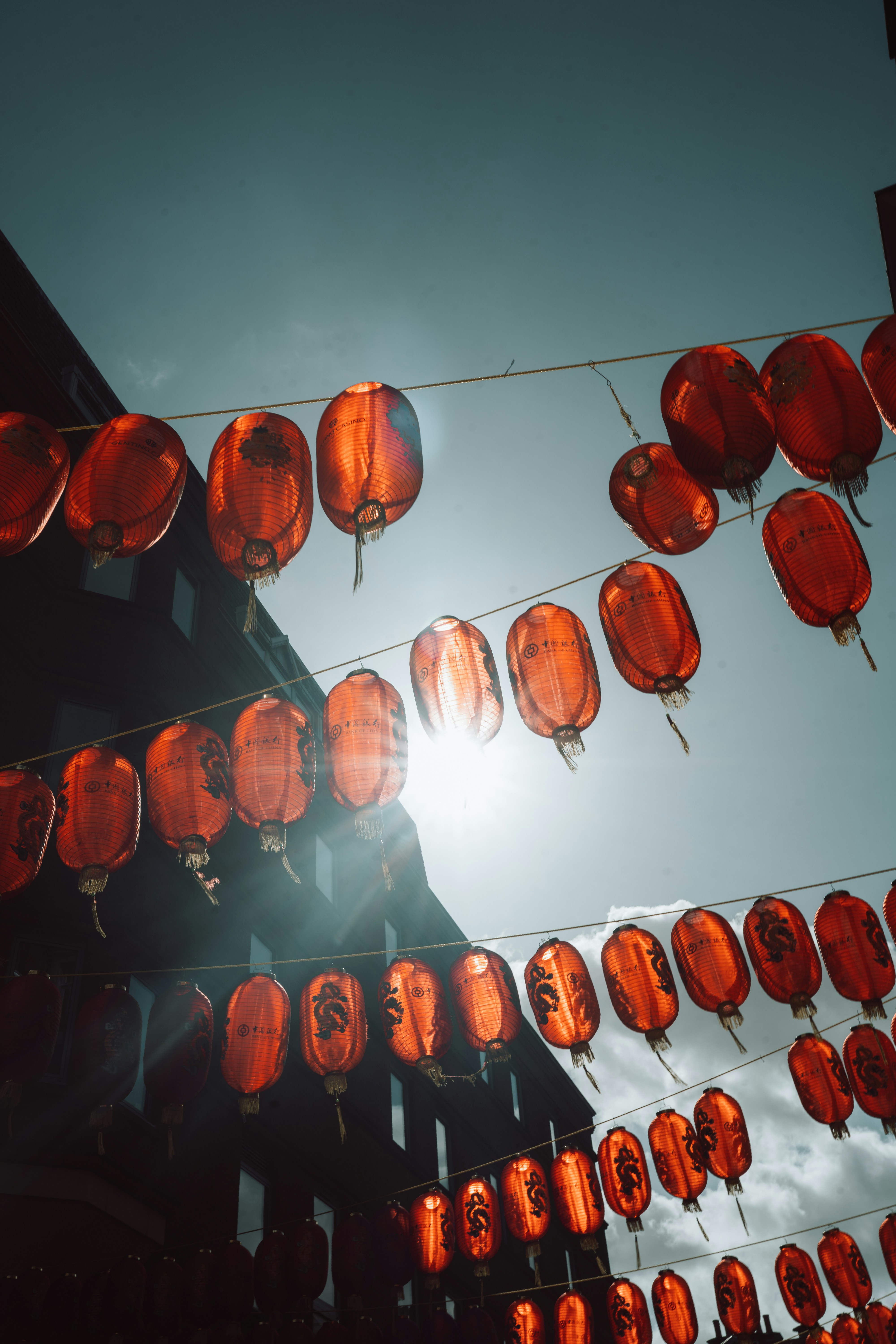 Sunlight streams through red lanterns hanging over a street.