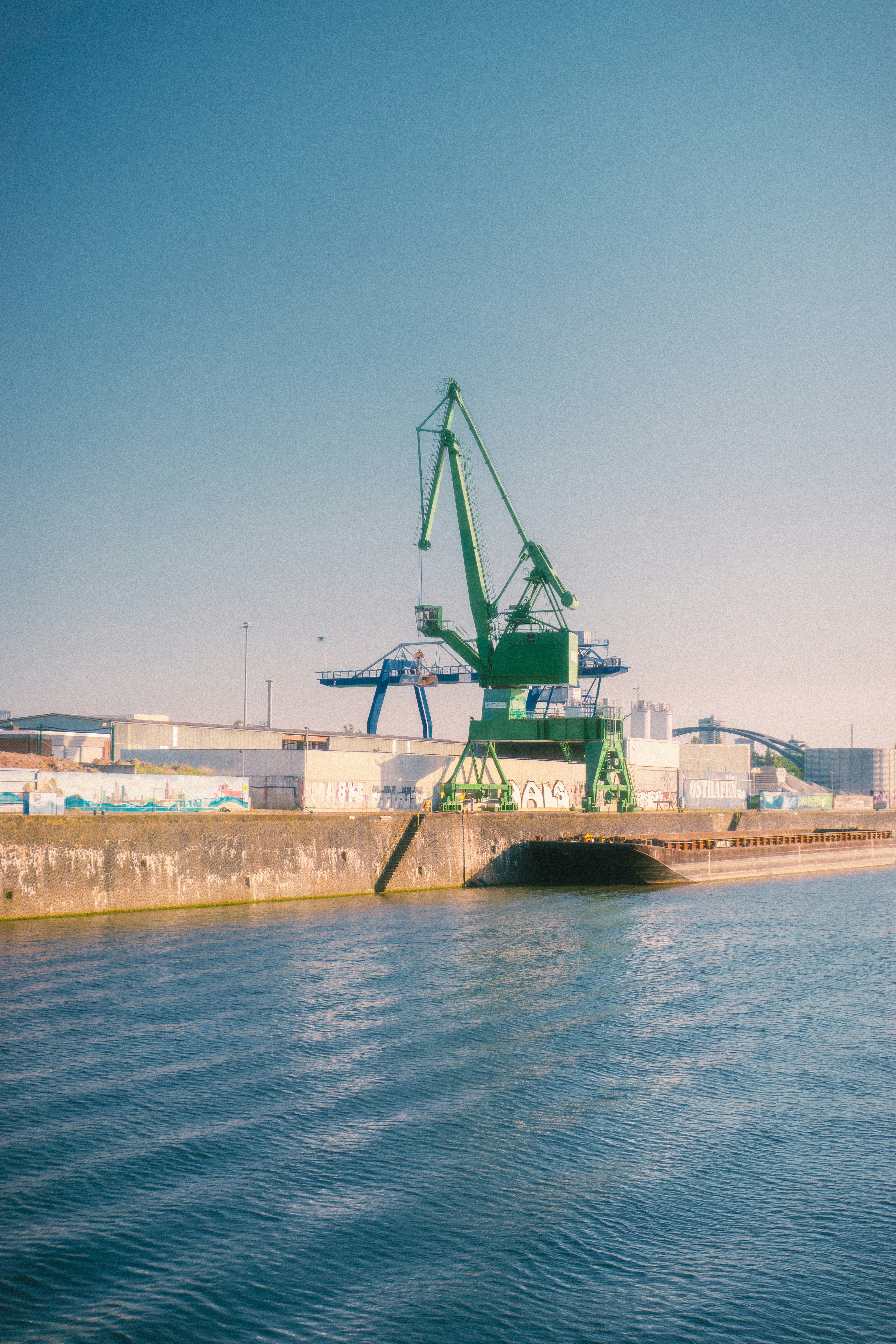 Green port crane overlooking rippled water under a clear sky.