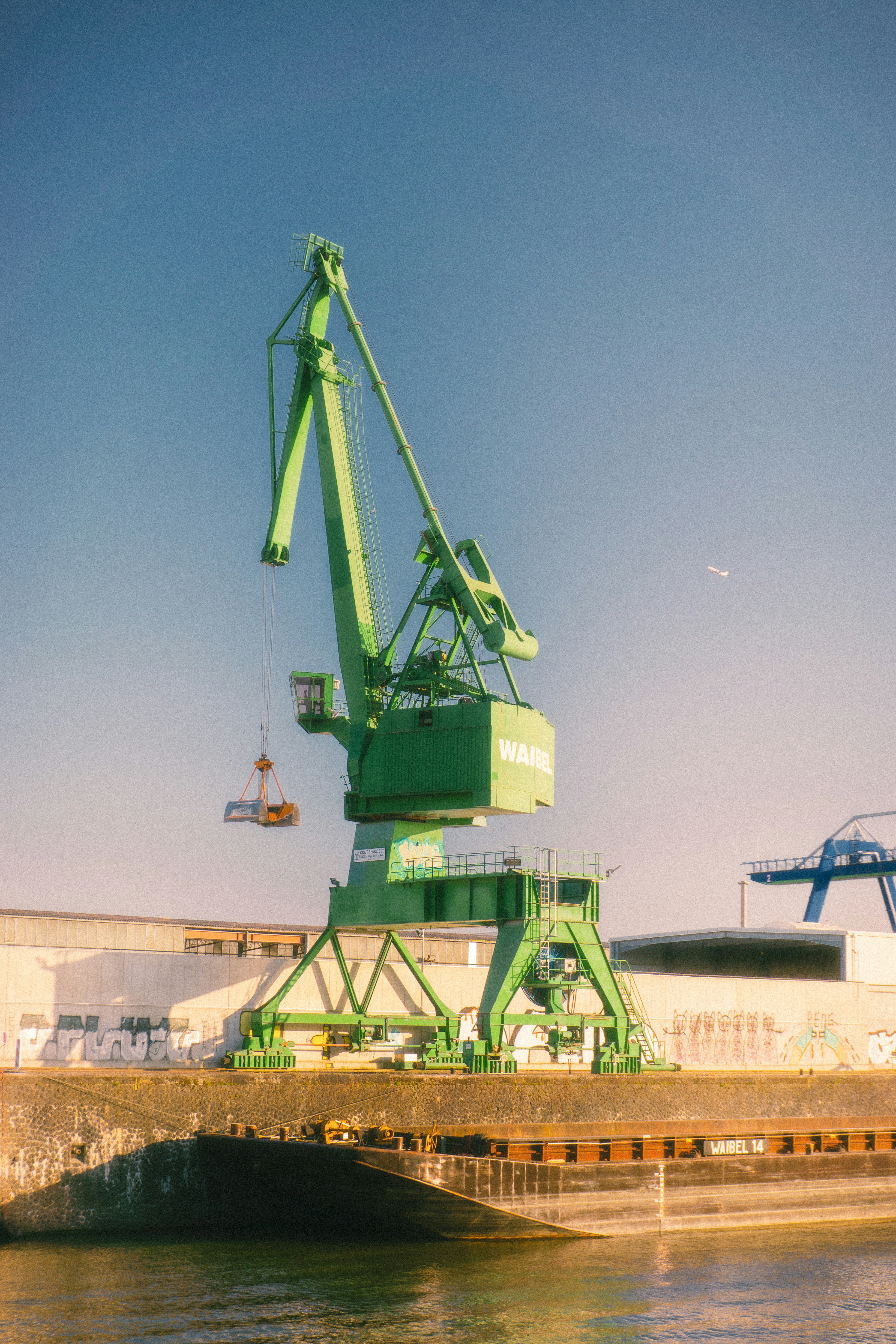 Green port crane lifts cargo against a clear blue sky.