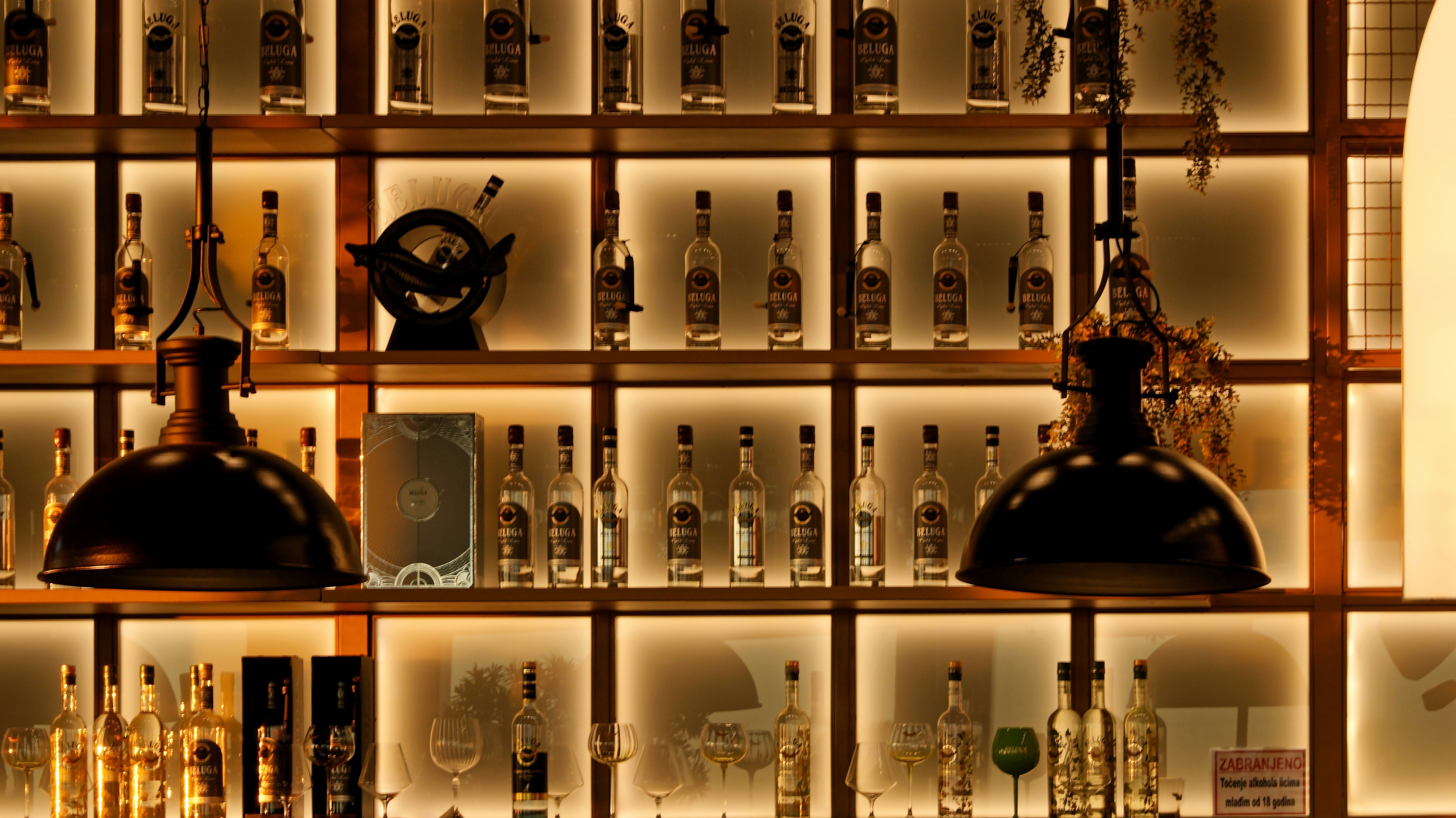 Illuminated bar shelf with many bottles and two large lamps.