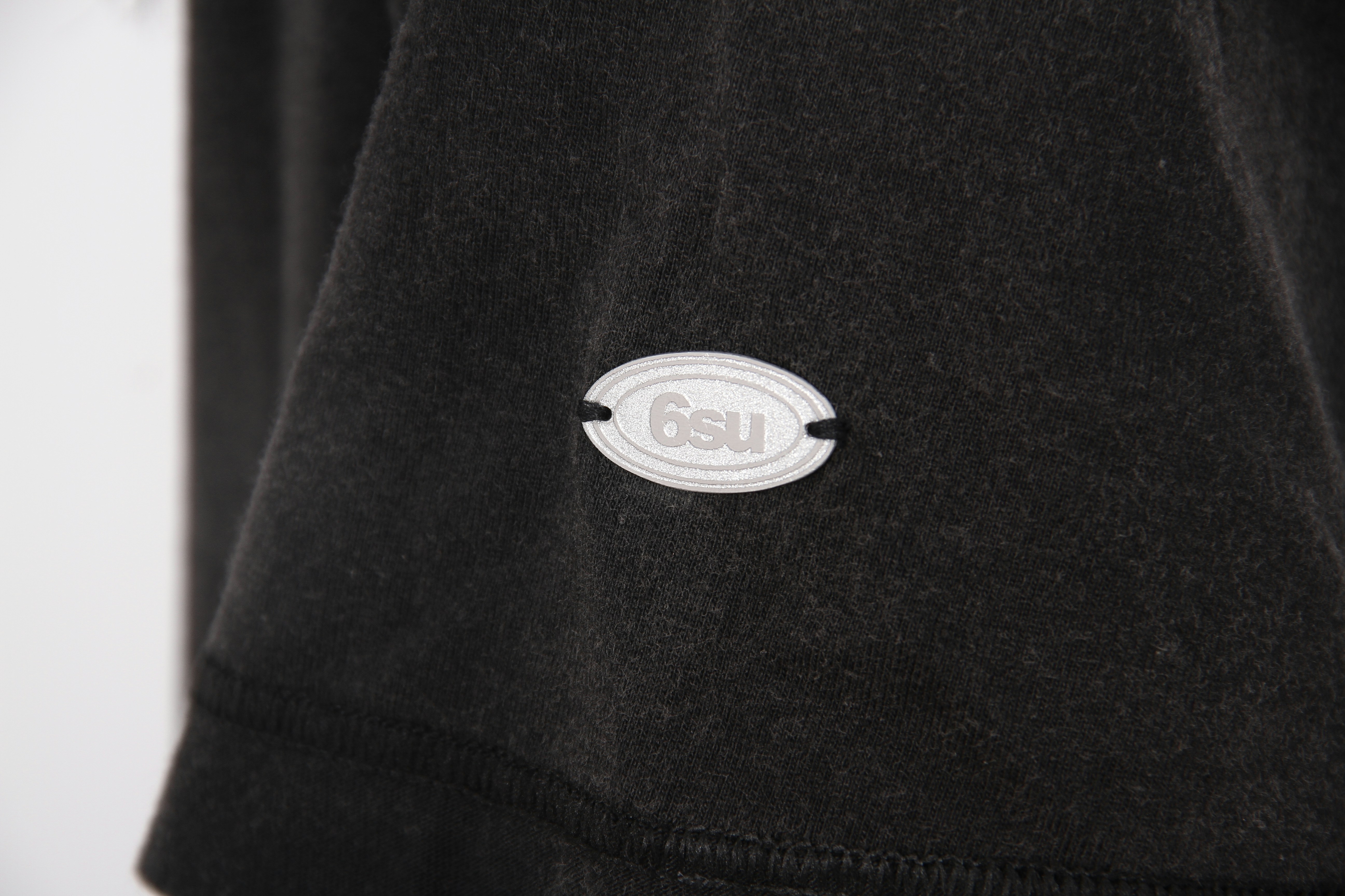 White '6su' label on dark, textured fabric
