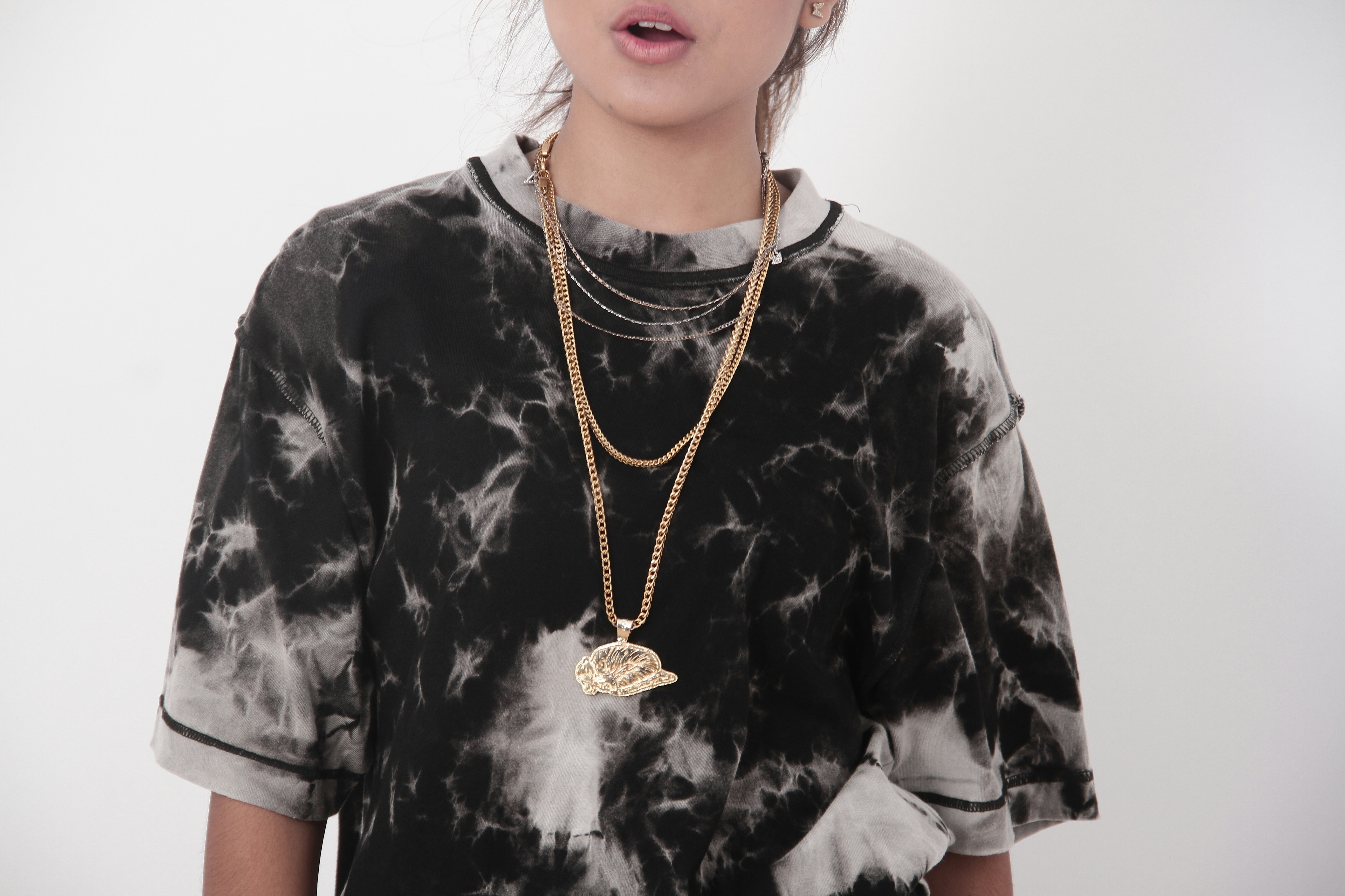 A person wearing a tie-dye shirt and layered gold chains