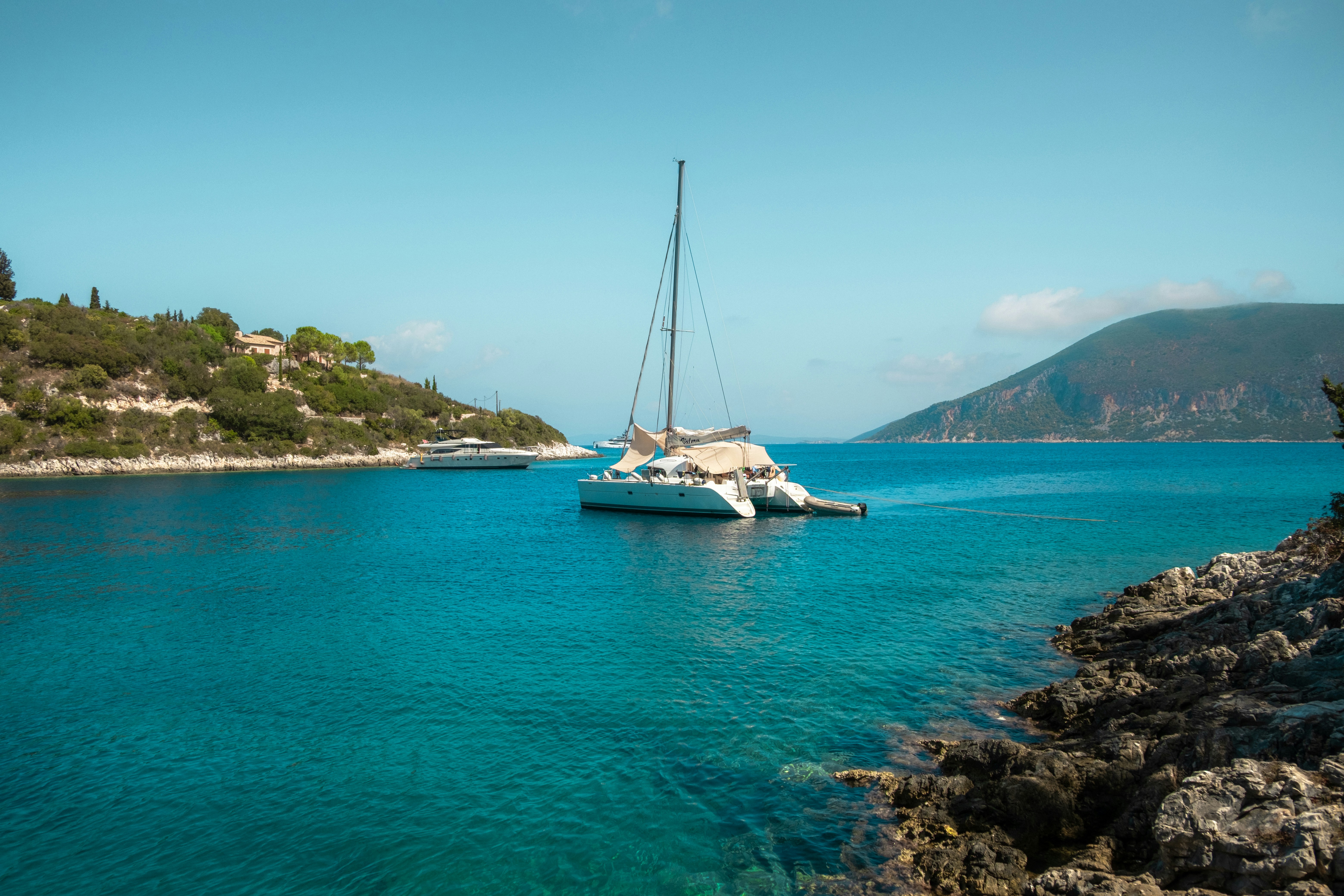 Catamaran in clear blue water by rocky shore.