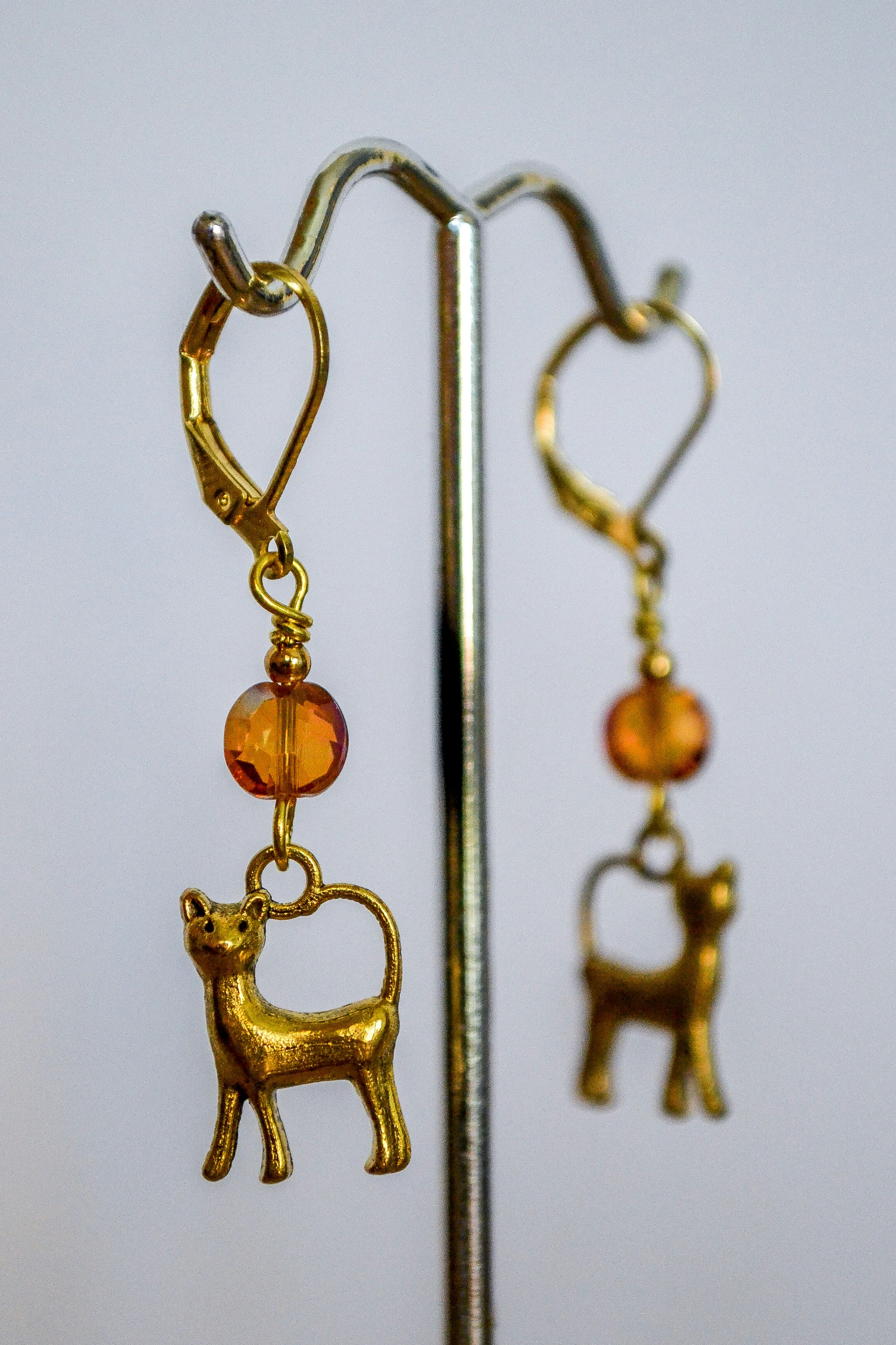 Gold cat earrings with orange beads on a display stand.