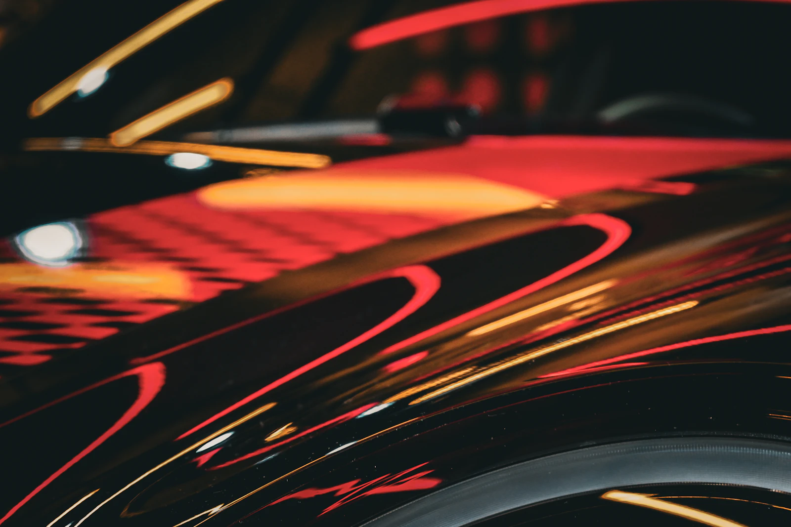 Glossy black car paint reflecting streaks of orange and red light