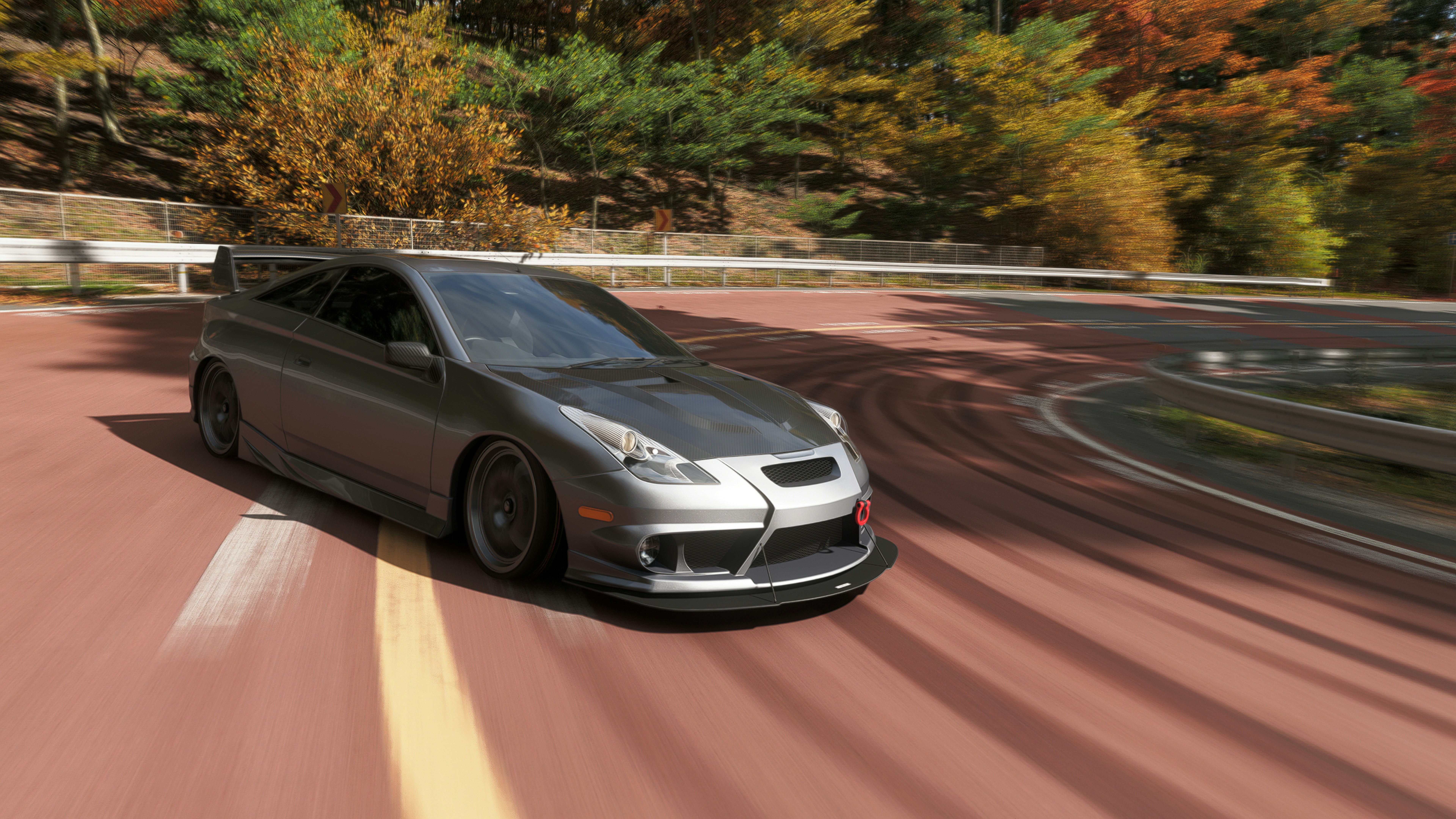 Silver sports car on a winding autumn road.