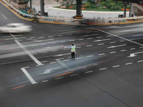 Person stands in busy urban intersection with blurred moving cars