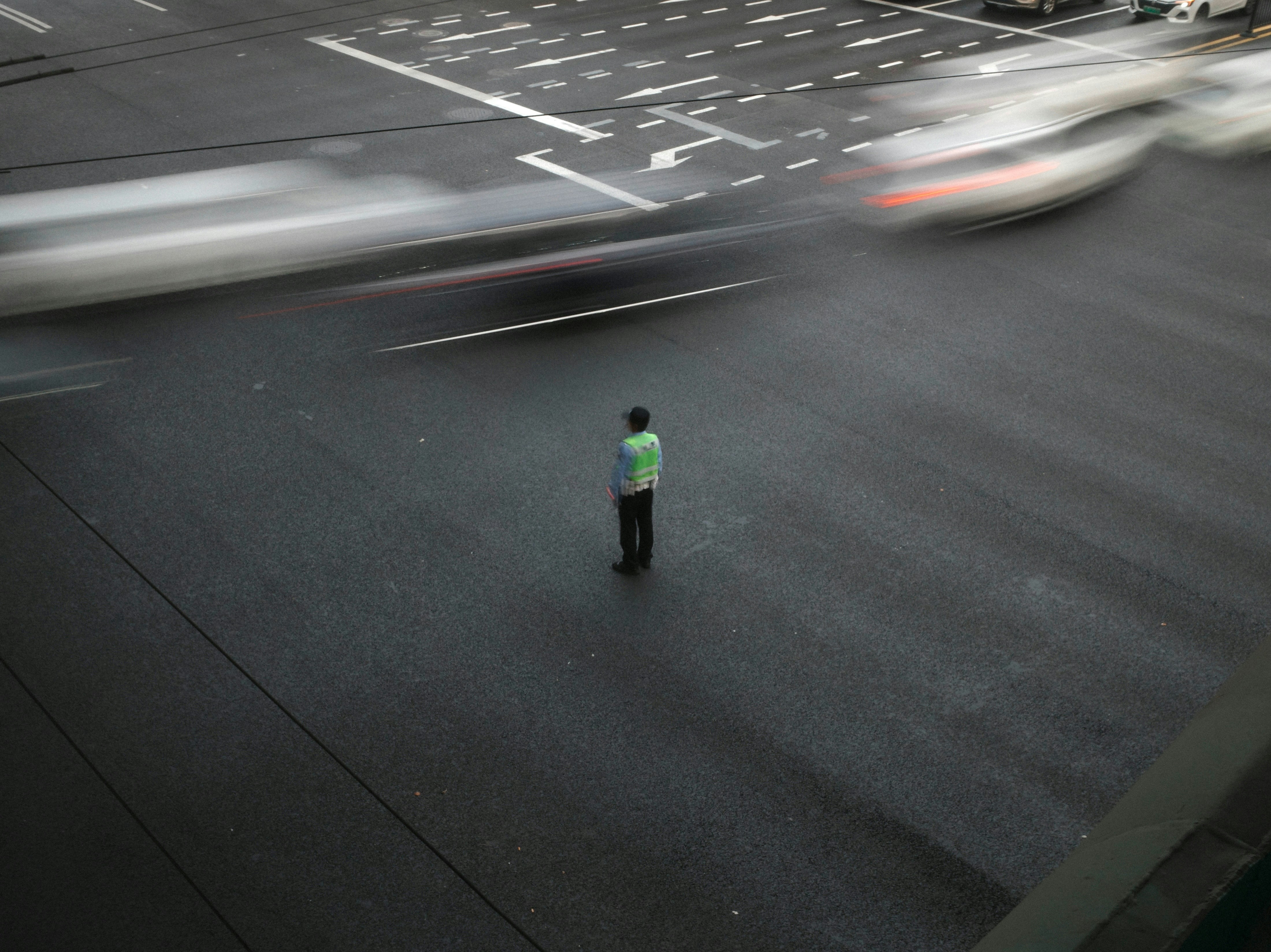 Lone figure in a street intersection with blurred traffic.