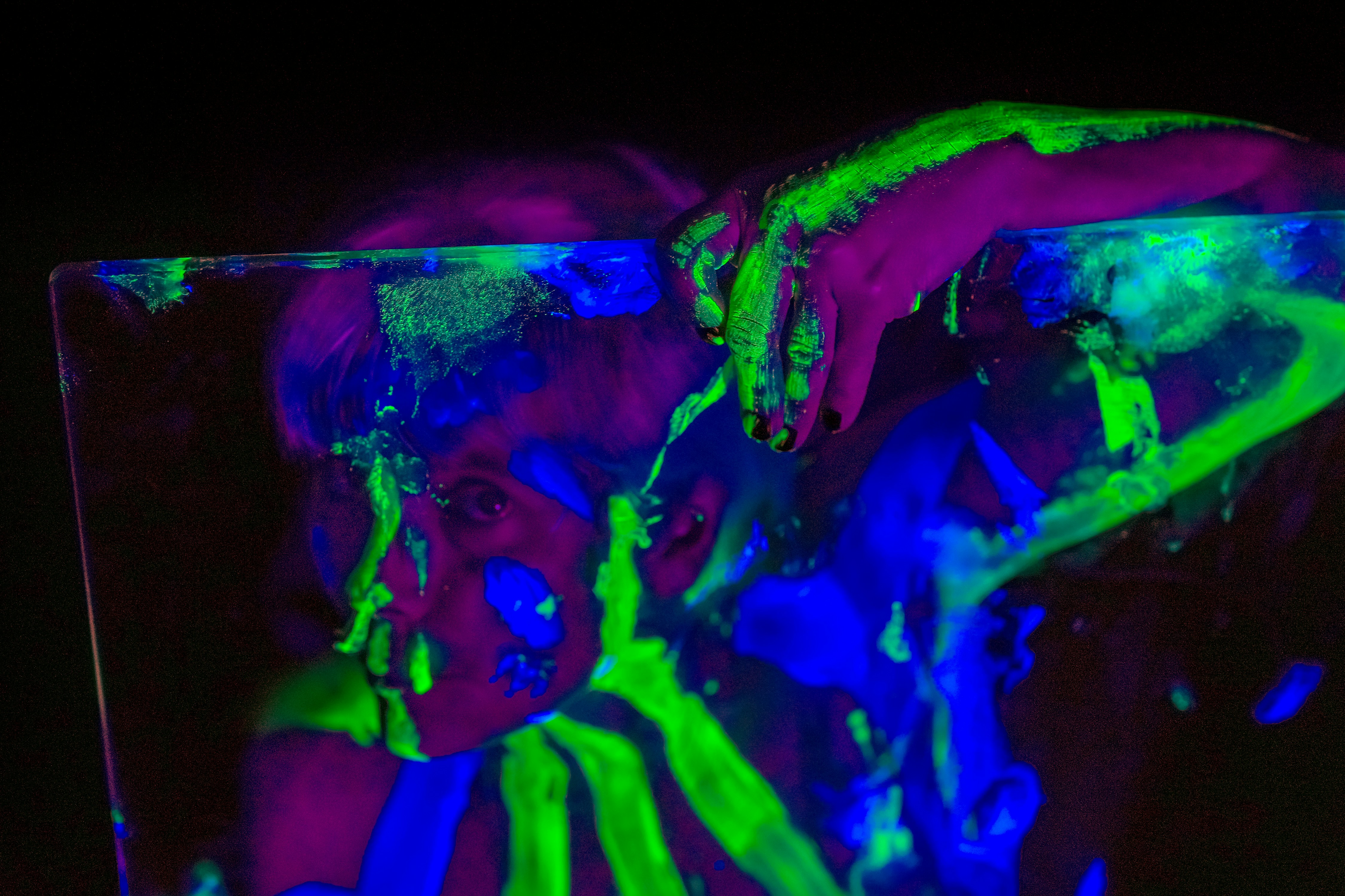 Close-up of a canvas covered in glowing neon paint splashes under UV light