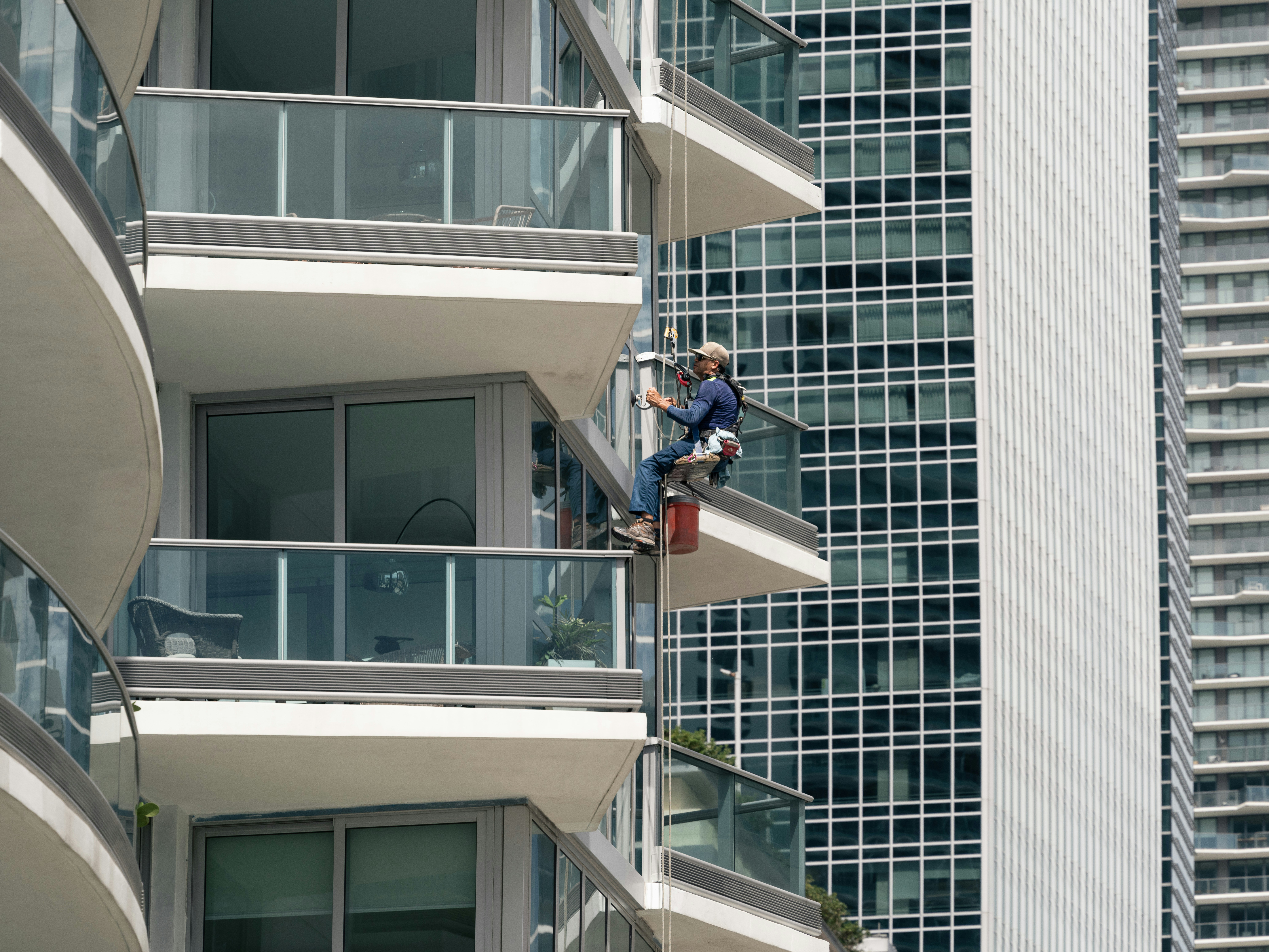 A window cleaner rappelling down a modern high-rise building.