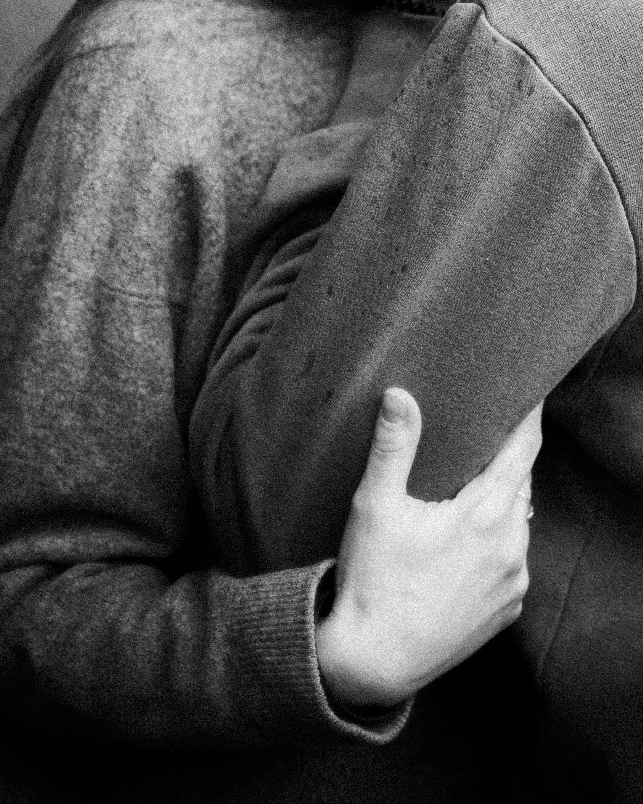 Hand holding another person's arm, both wearing sweaters.