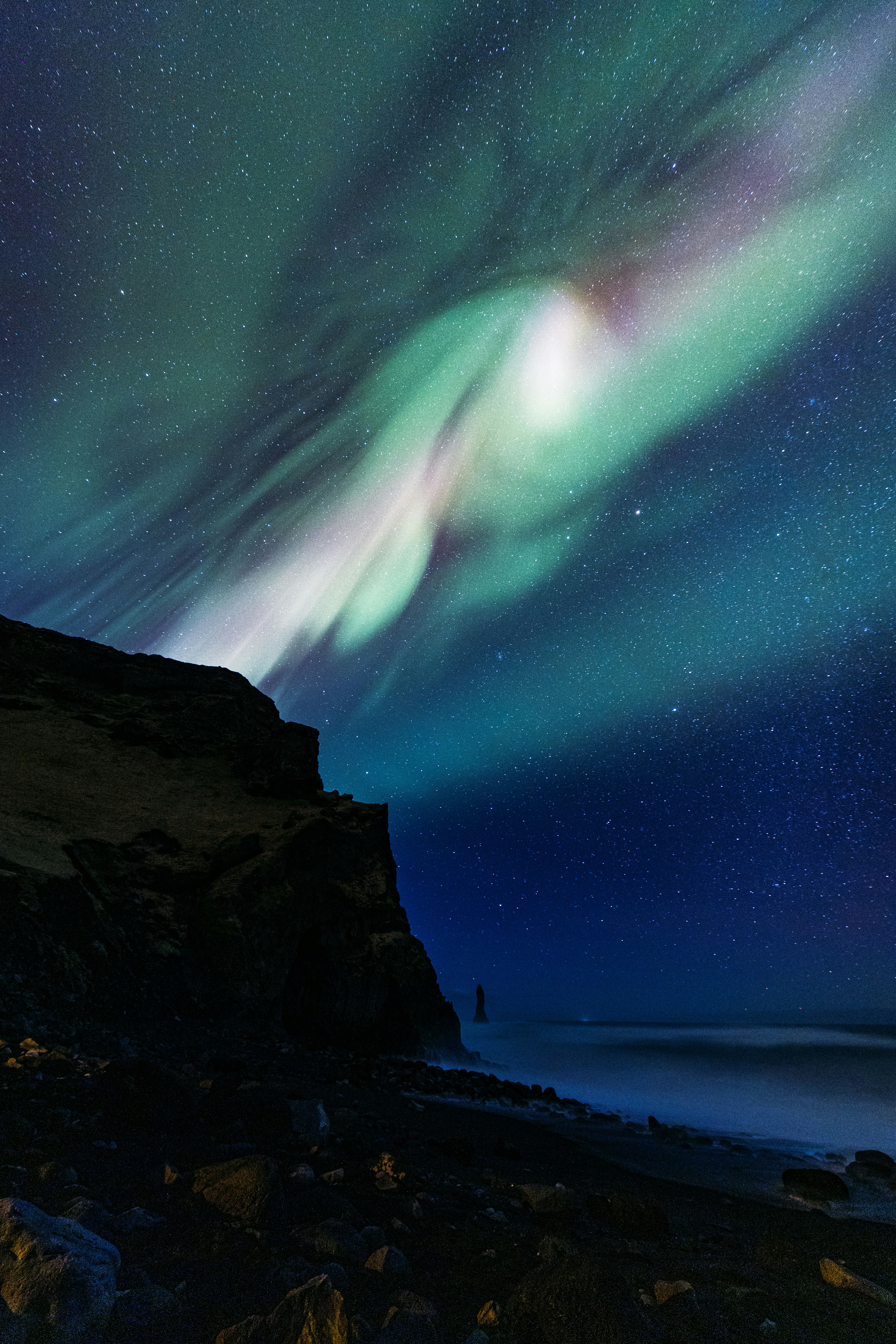 Aurora borealis illuminates dark night sky over ocean and cliffs. - 相关推荐