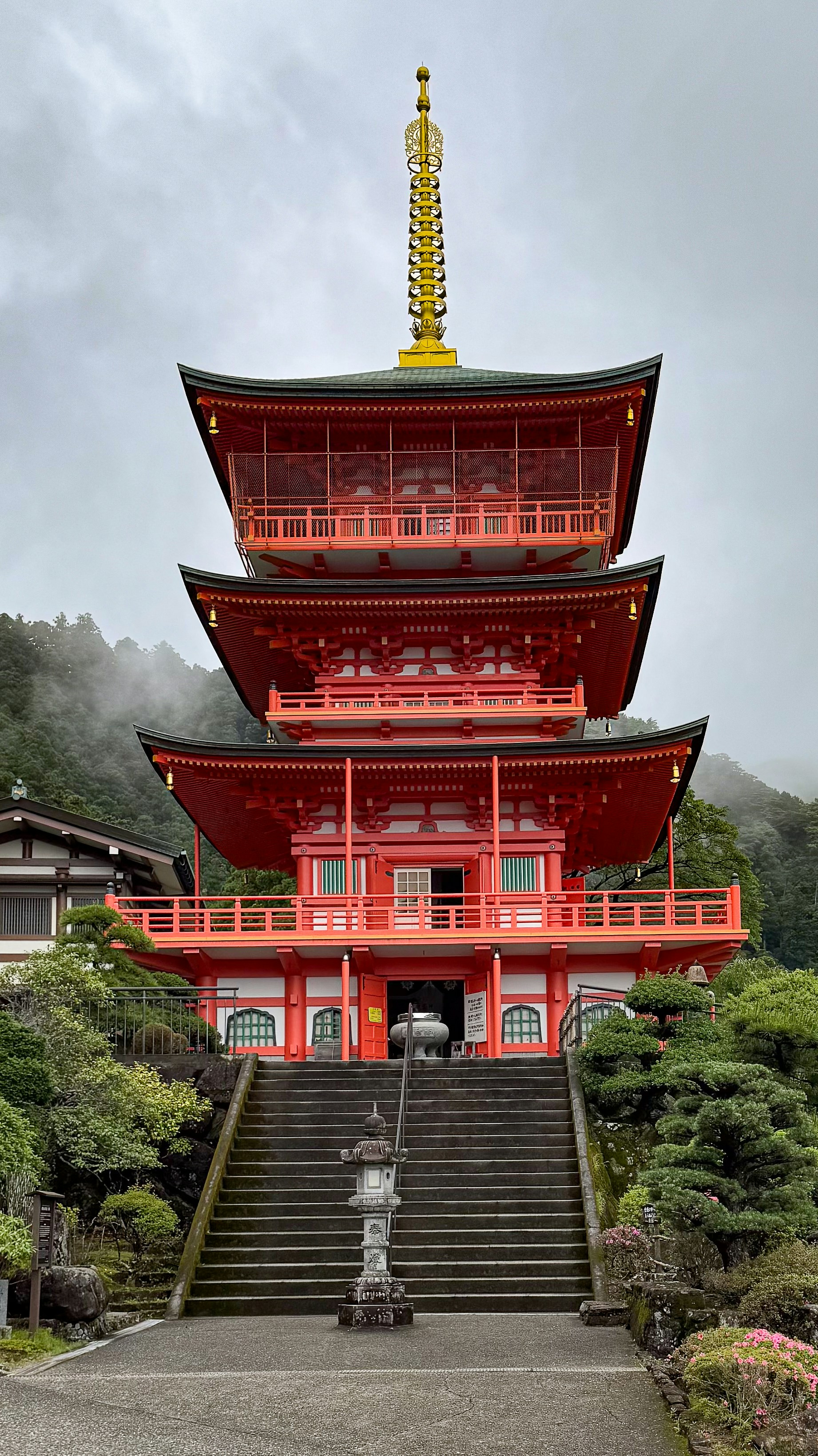 Pagoda japonesa con escaleras rodeadas de vegetación y montañas brumosas.