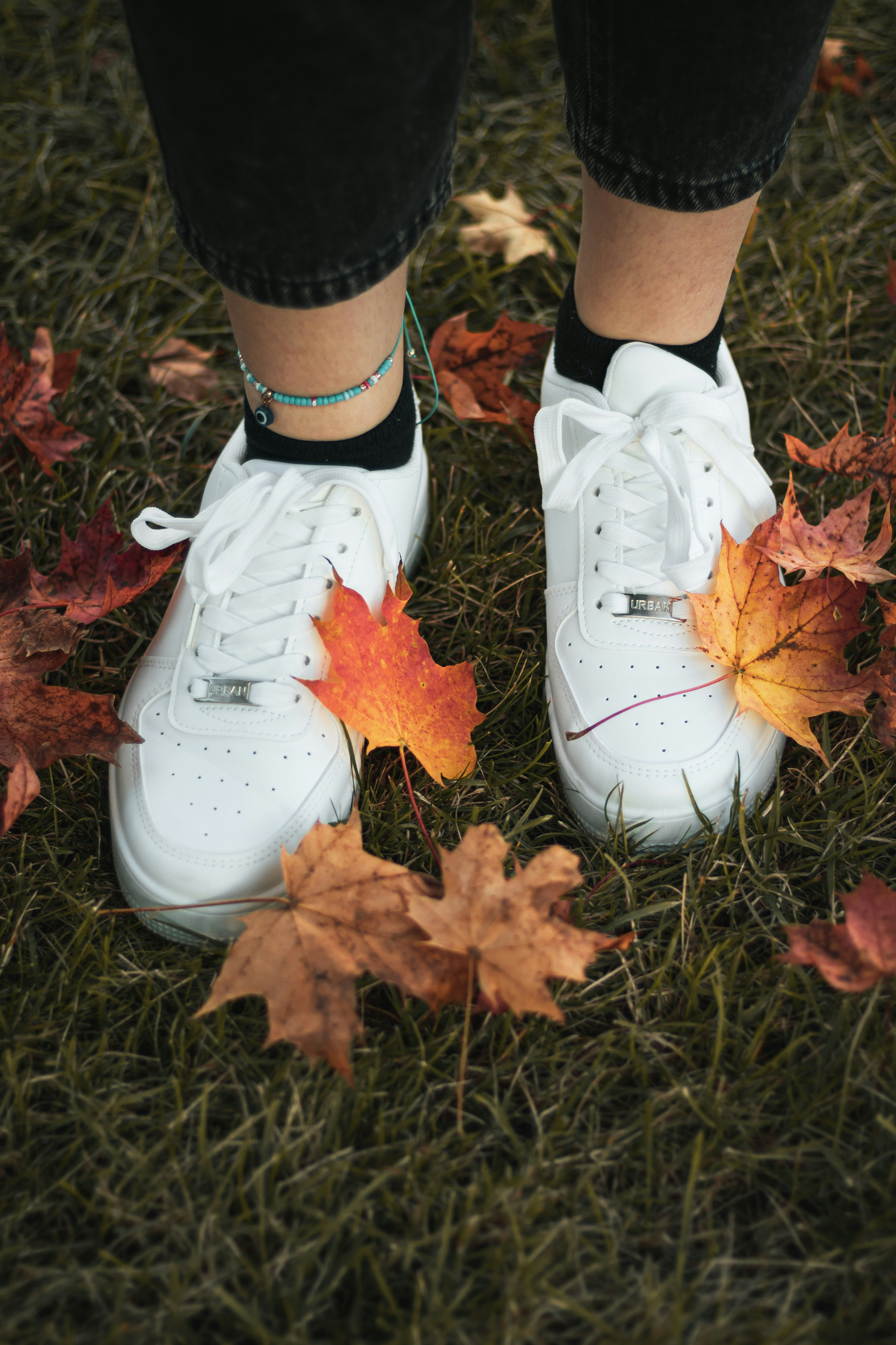 White sneakers on grass with colorful autumn leaves.