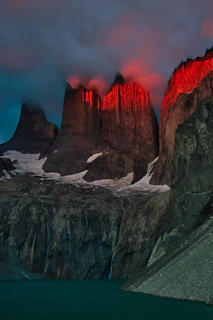 The Cordillera del Paine peaks glowing red under low light above a glacial lake