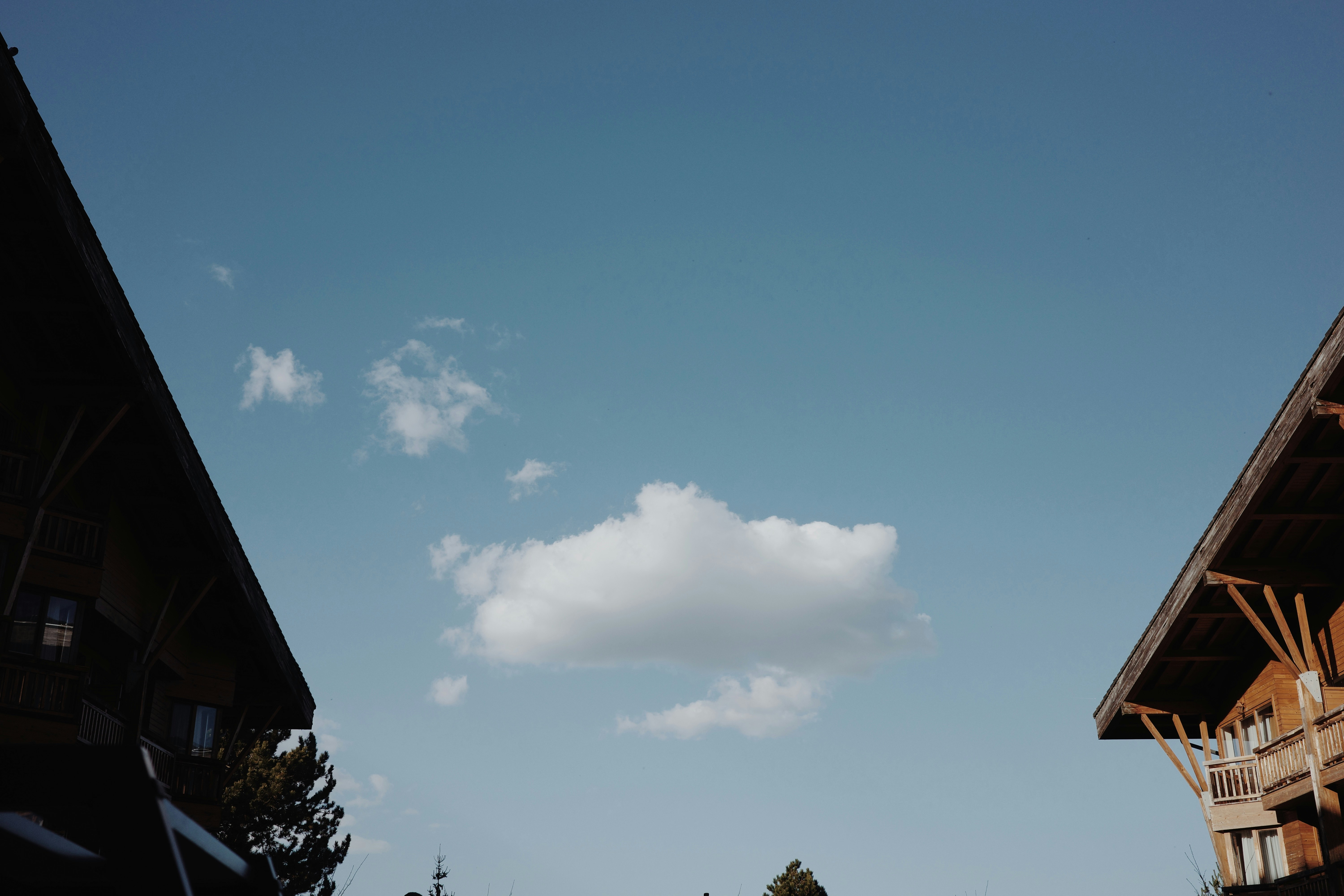 Langit biru dengan awan putih di antara dua bangunan kayu.