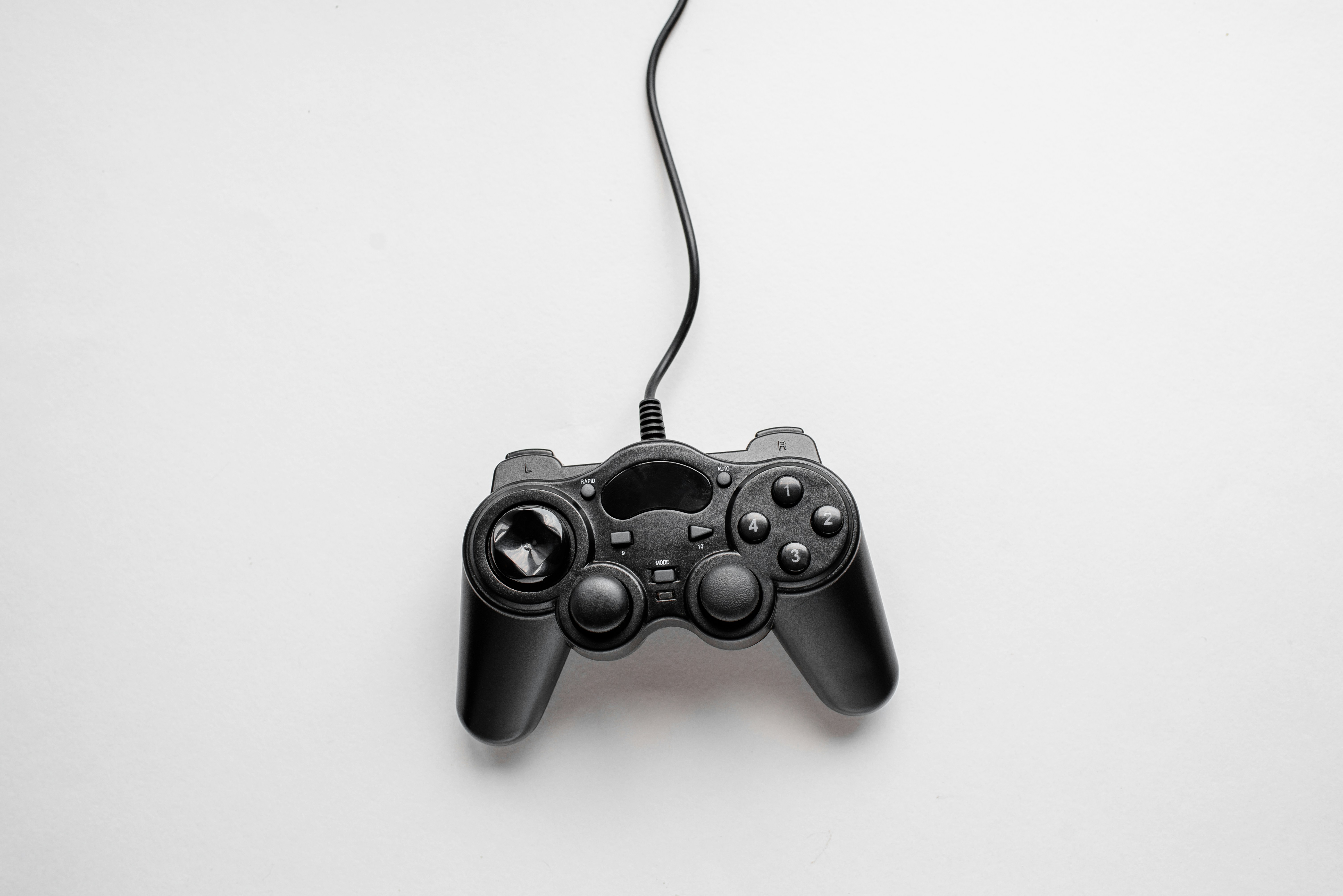 Un mando de juego con cable negro sobre fondo blanco.