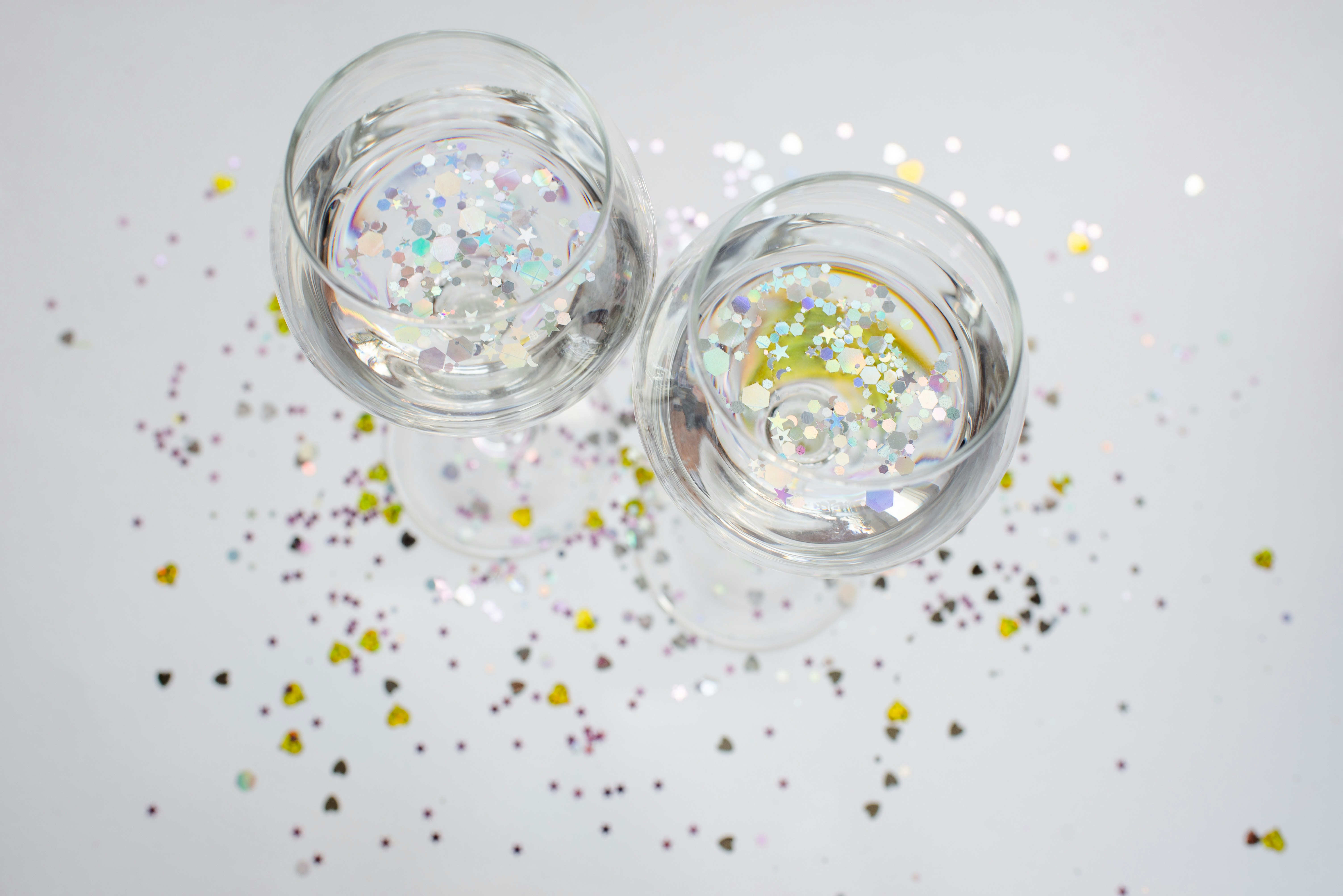 Dos vasos con purpurina y confeti sobre fondo blanco.