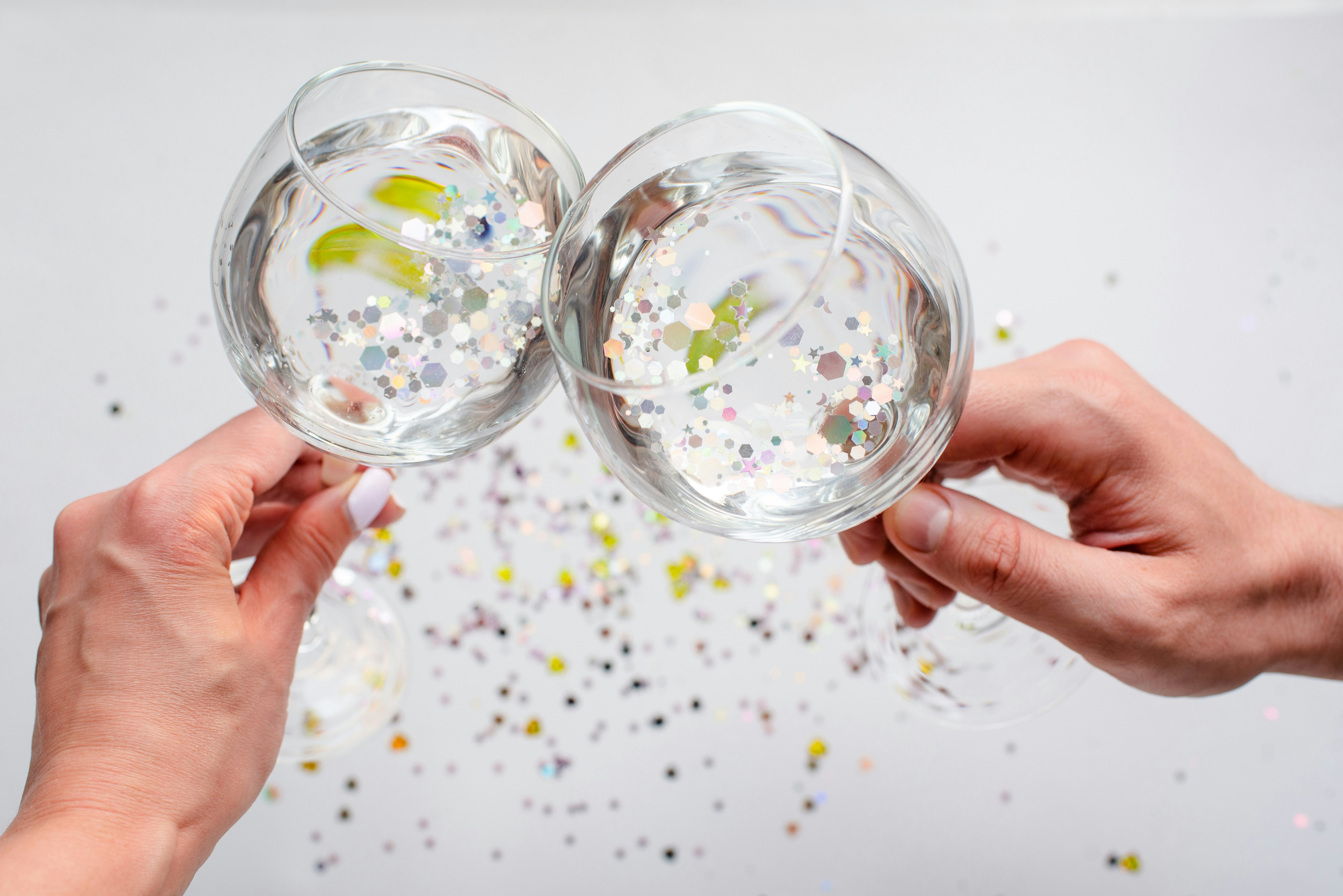 Dos manos sujetando copas de vino con confeti espumoso.