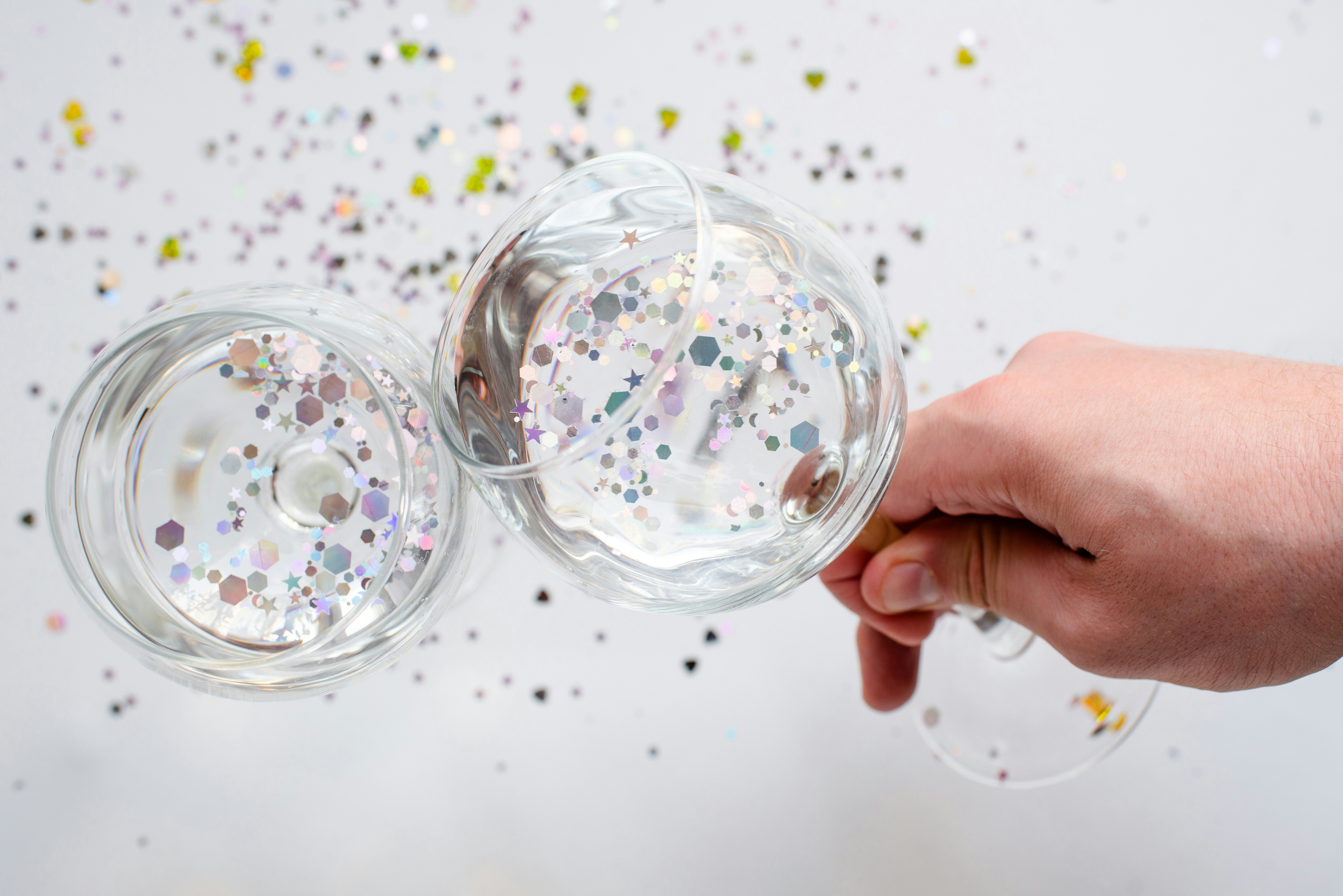 Dos vasos con purpurina brillante y una mano sobre blanco.