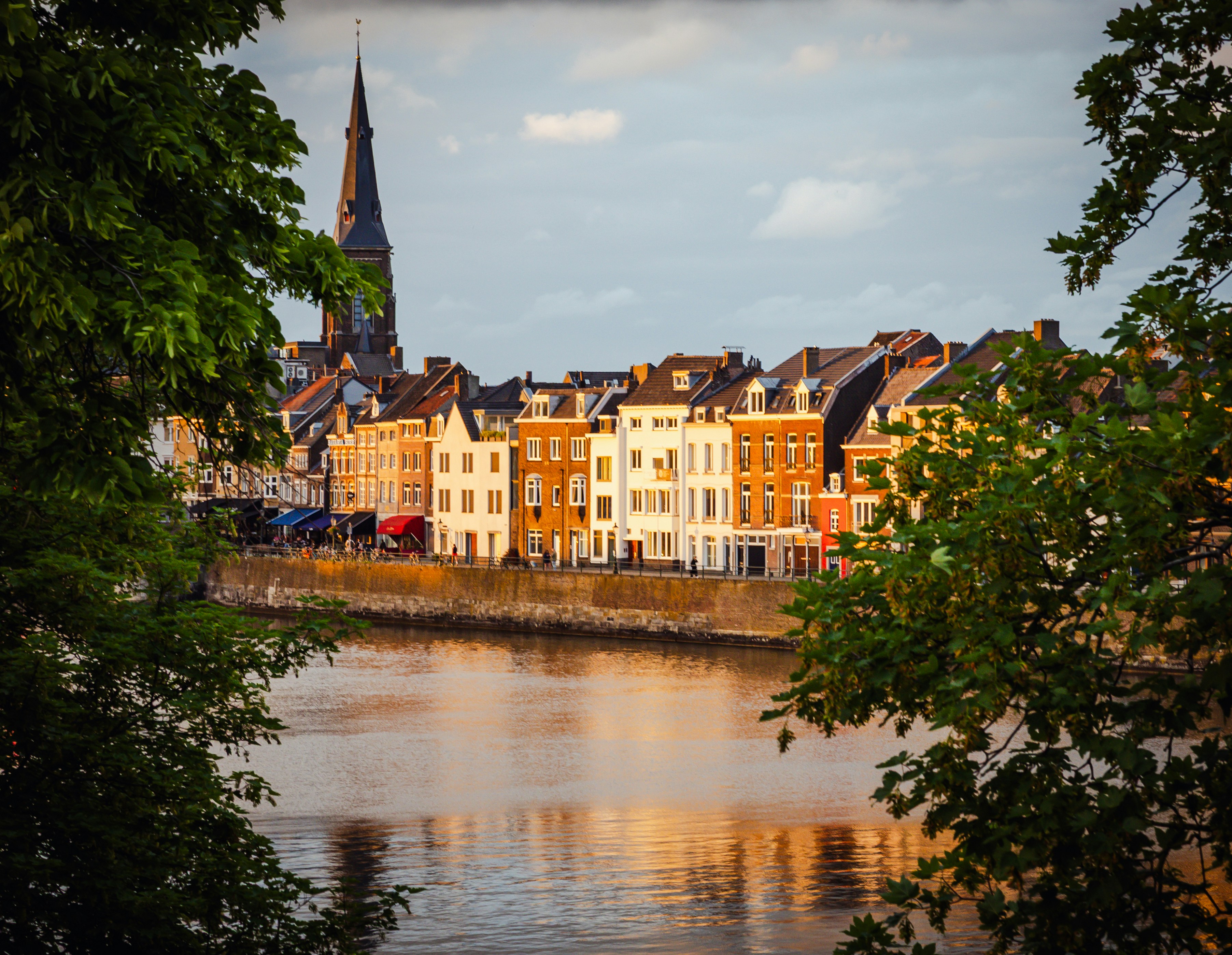 Riverfront town with historic buildings and church spire at sunset.
