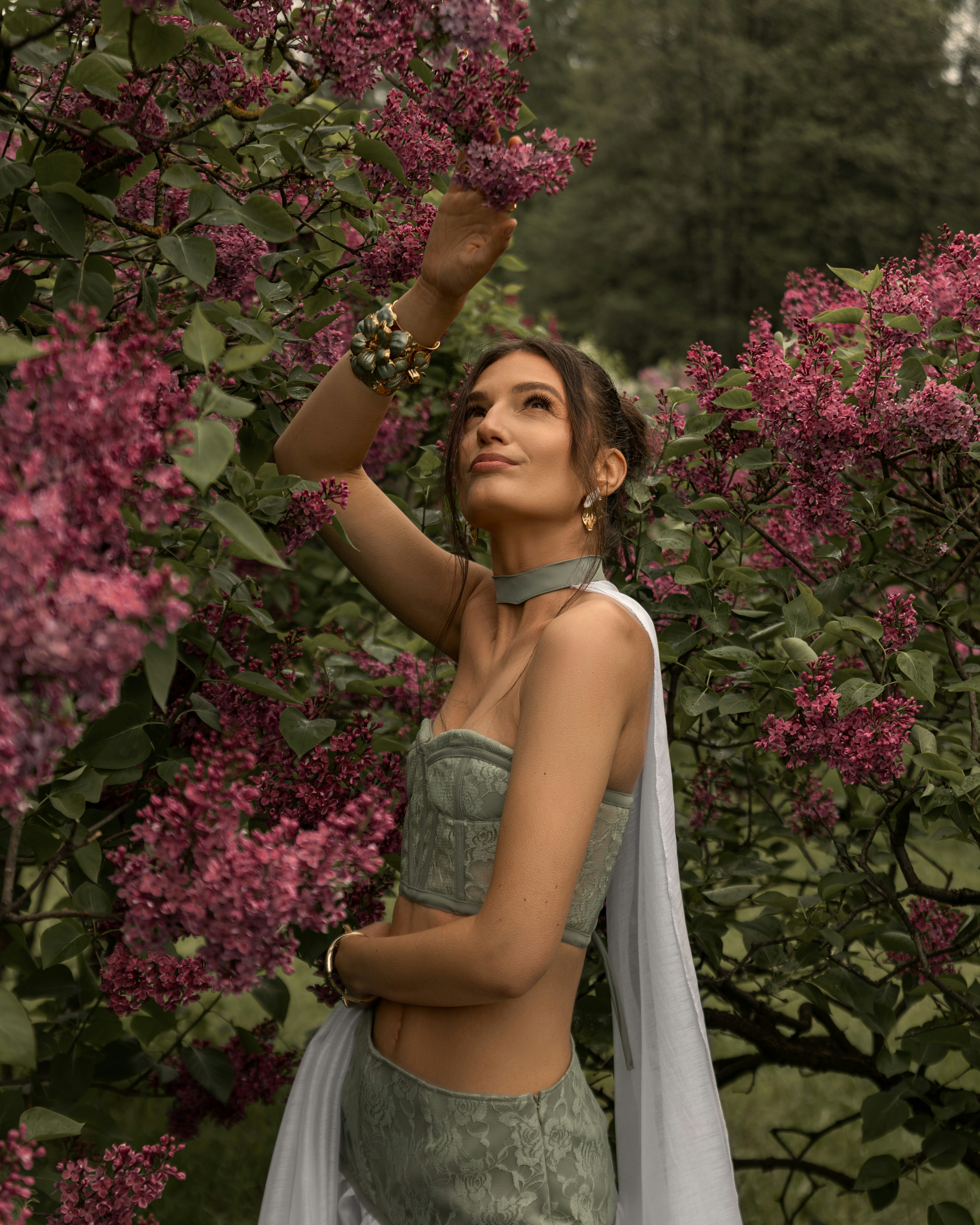 Jovem mulher com trajes tradicionais tocando flores de lilás roxo.