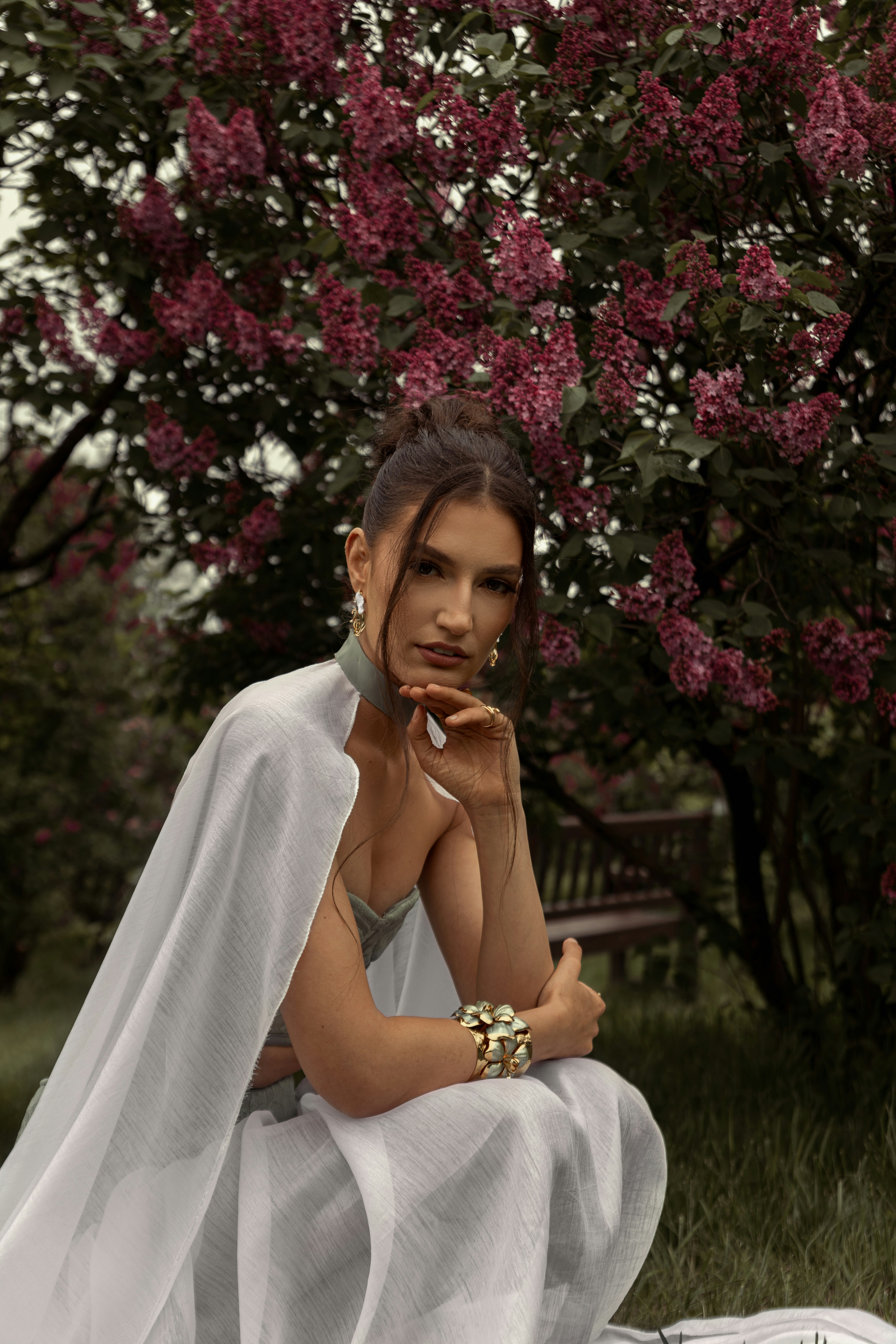 Mulher elegante posa ao lado de um arbusto de lilás roxo florido.