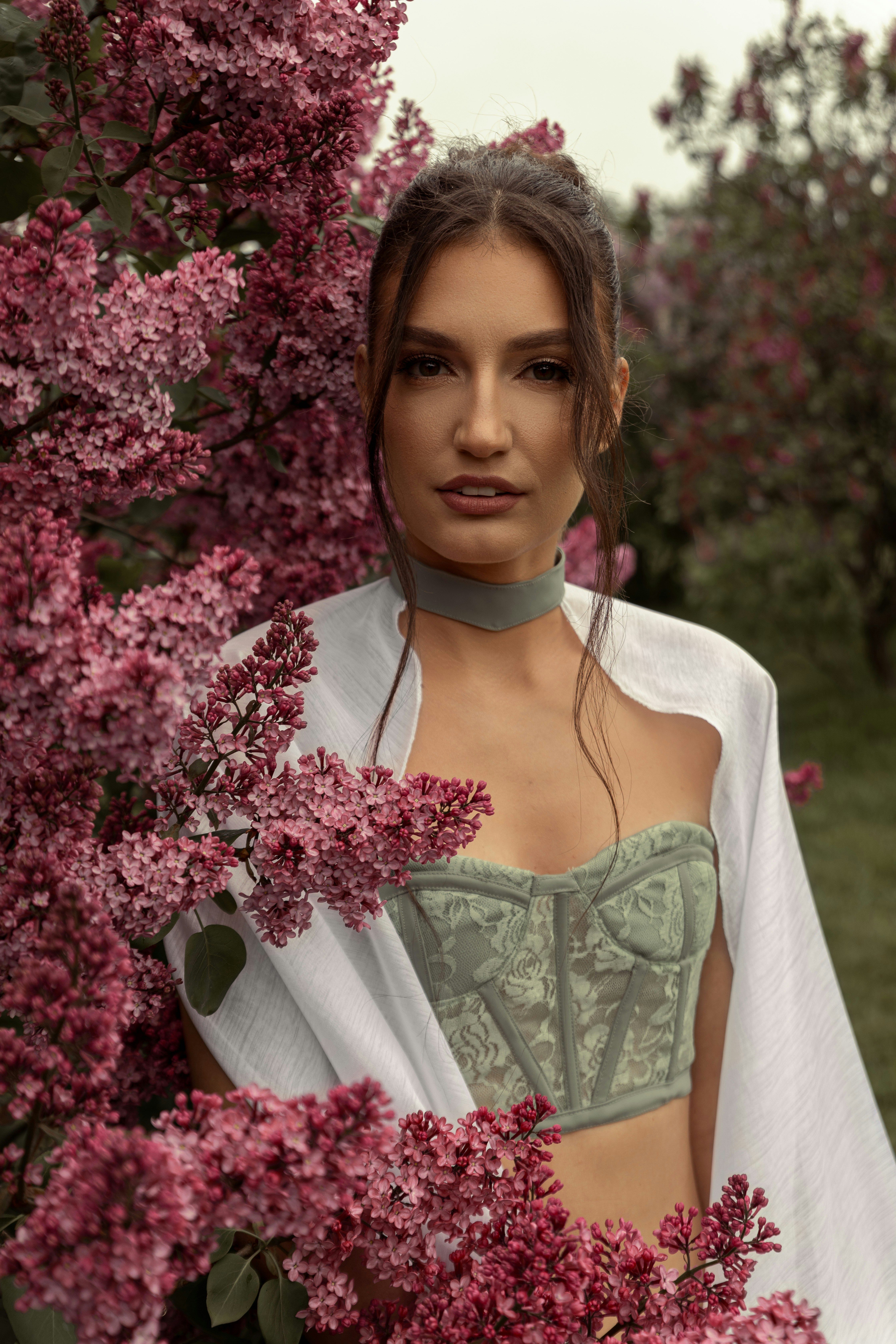 Mulher de blusa verde cercada por lindas flores de lilás roxo.