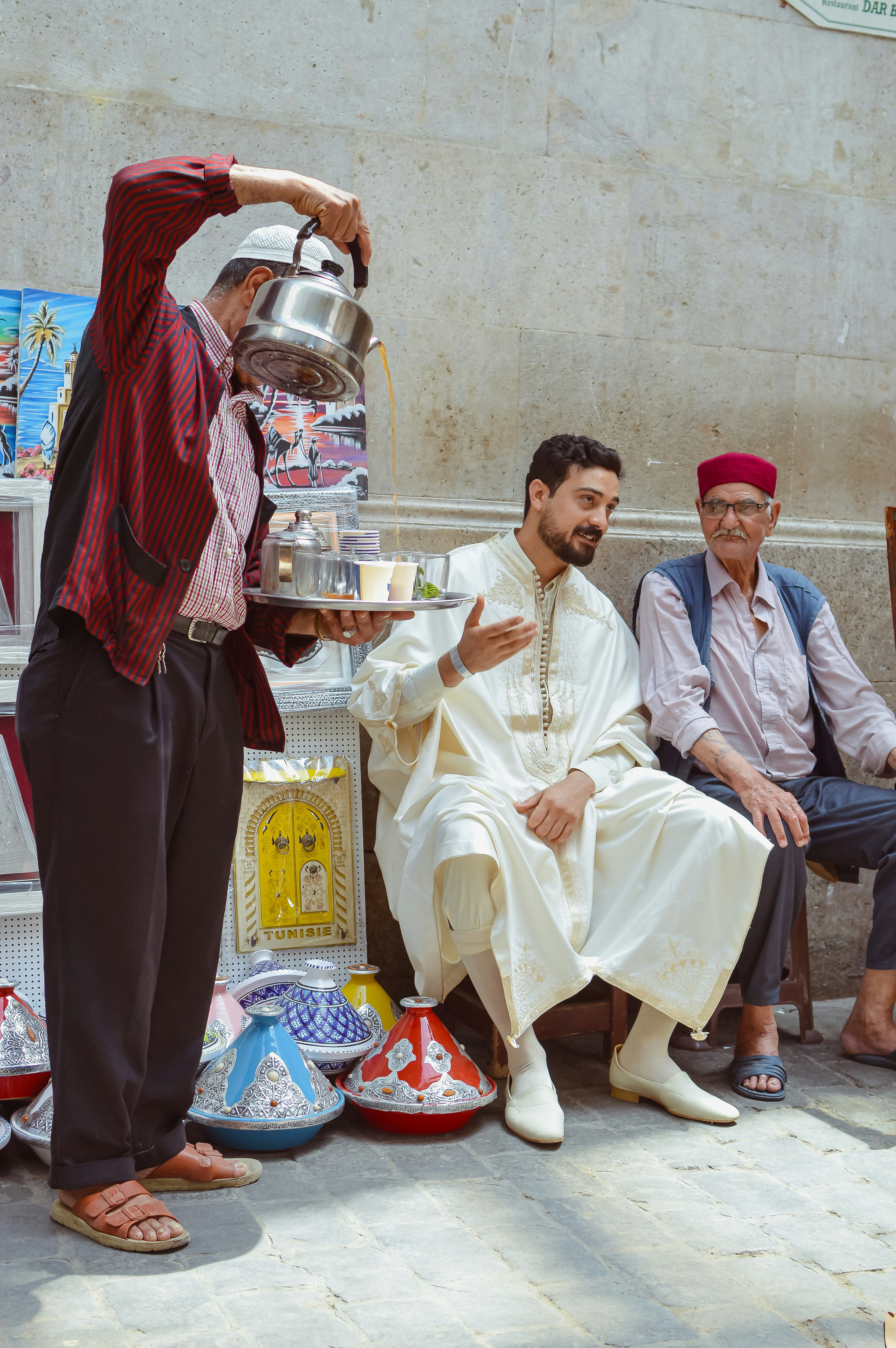A man pours tea for two men in traditional attire.