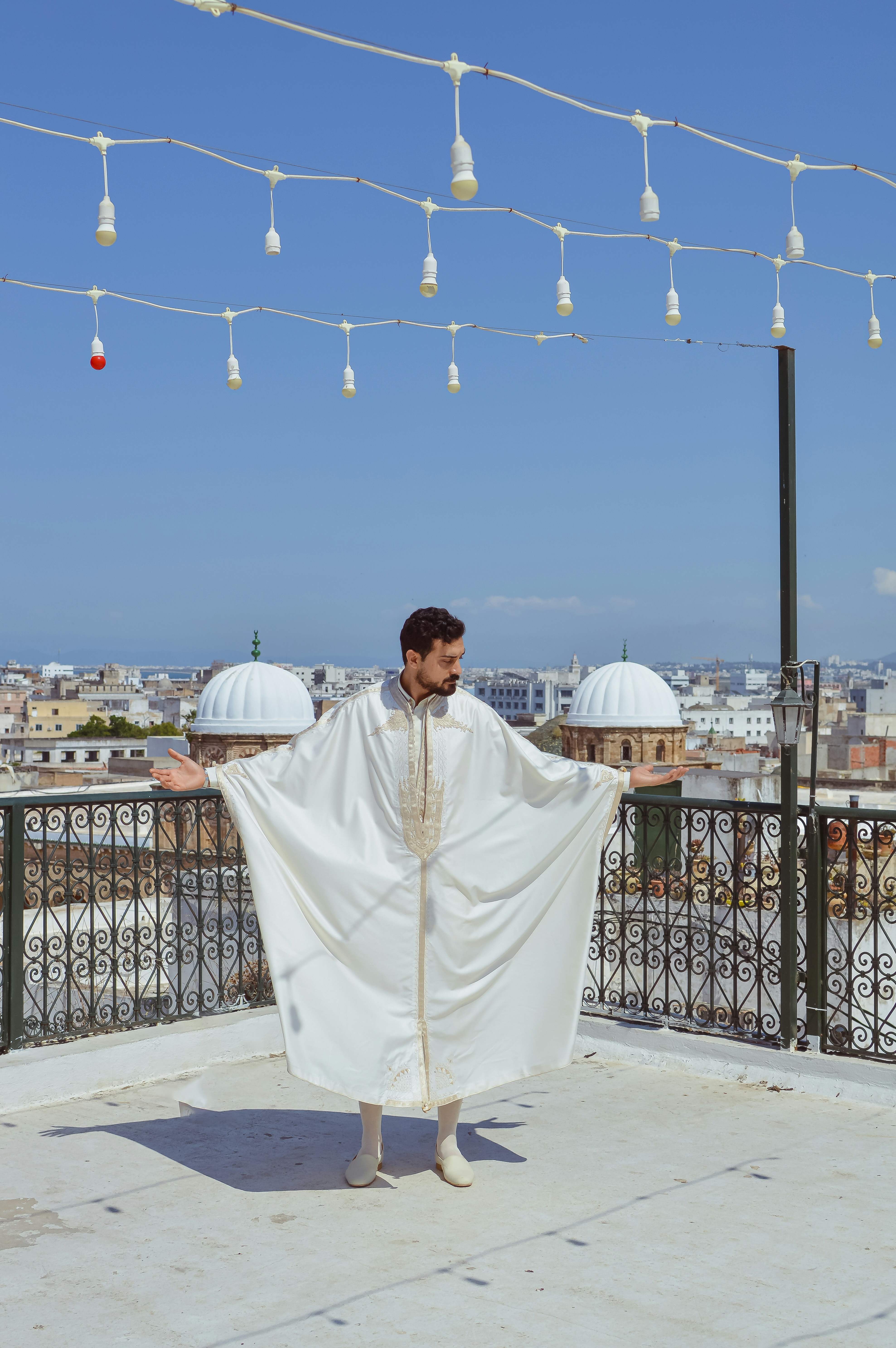 Man in white traditional attire on a rooftop overlooking city.