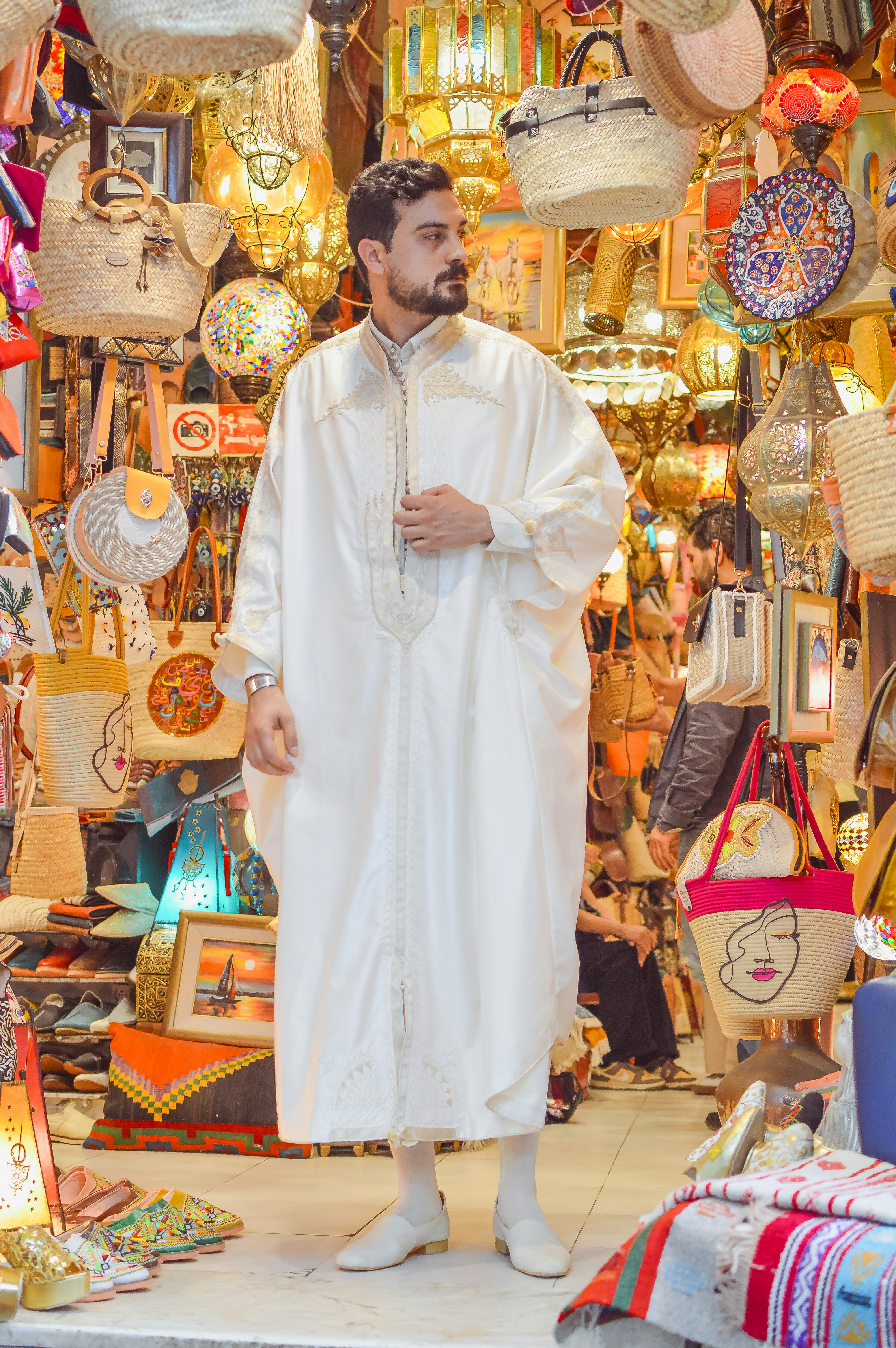 Man in traditional white garment amidst market crafts.