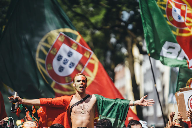 Enthusiastic man with portuguese flag cape and outstretched arms.