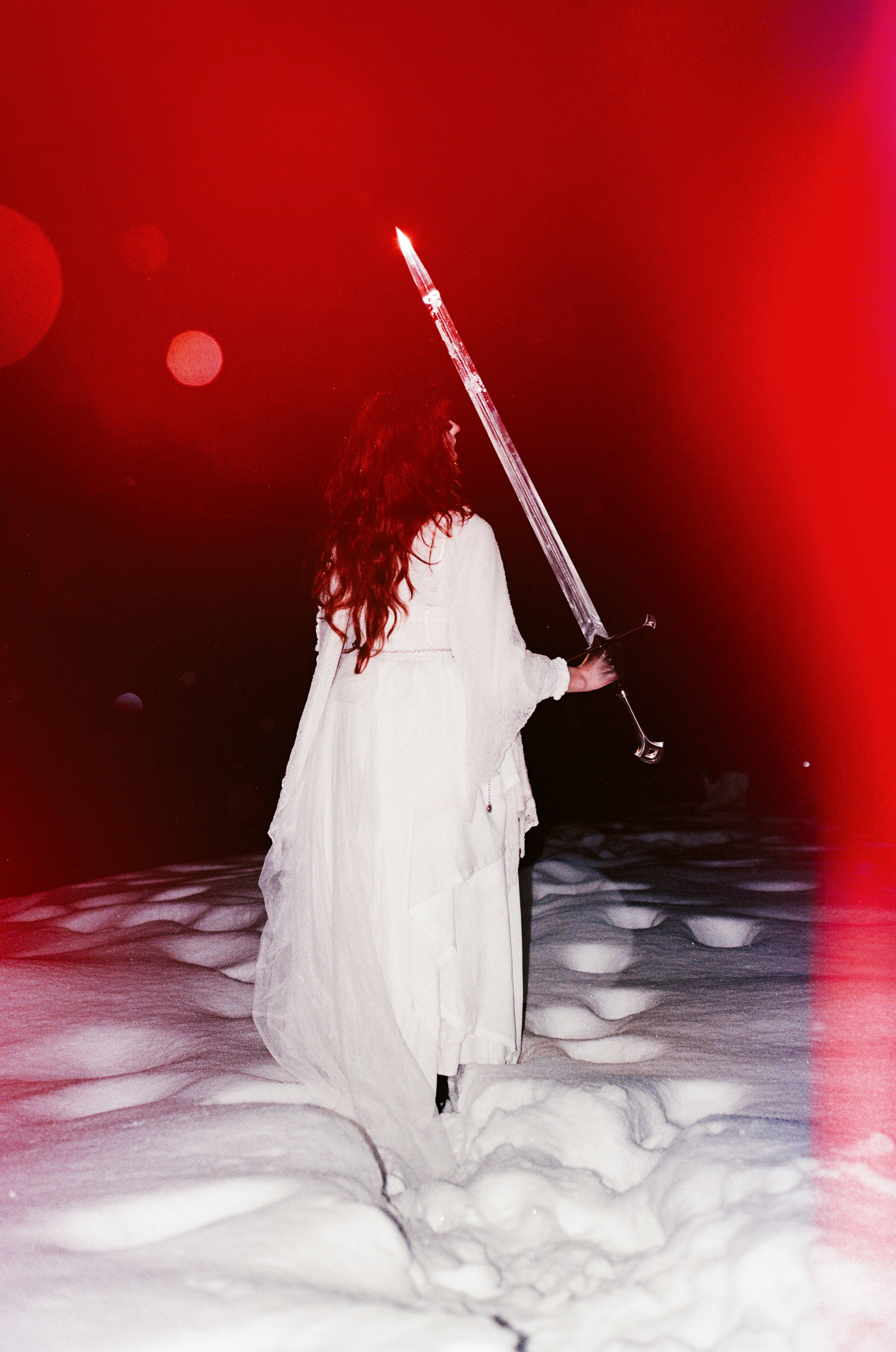 Woman in white holds glowing sword in snowy, red-lit landscape. - 相关推荐