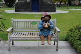 Paddington bear statue sits on a bench holding a sandwich
