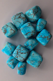 Polished turquoise stones with dark veins on a grey background.