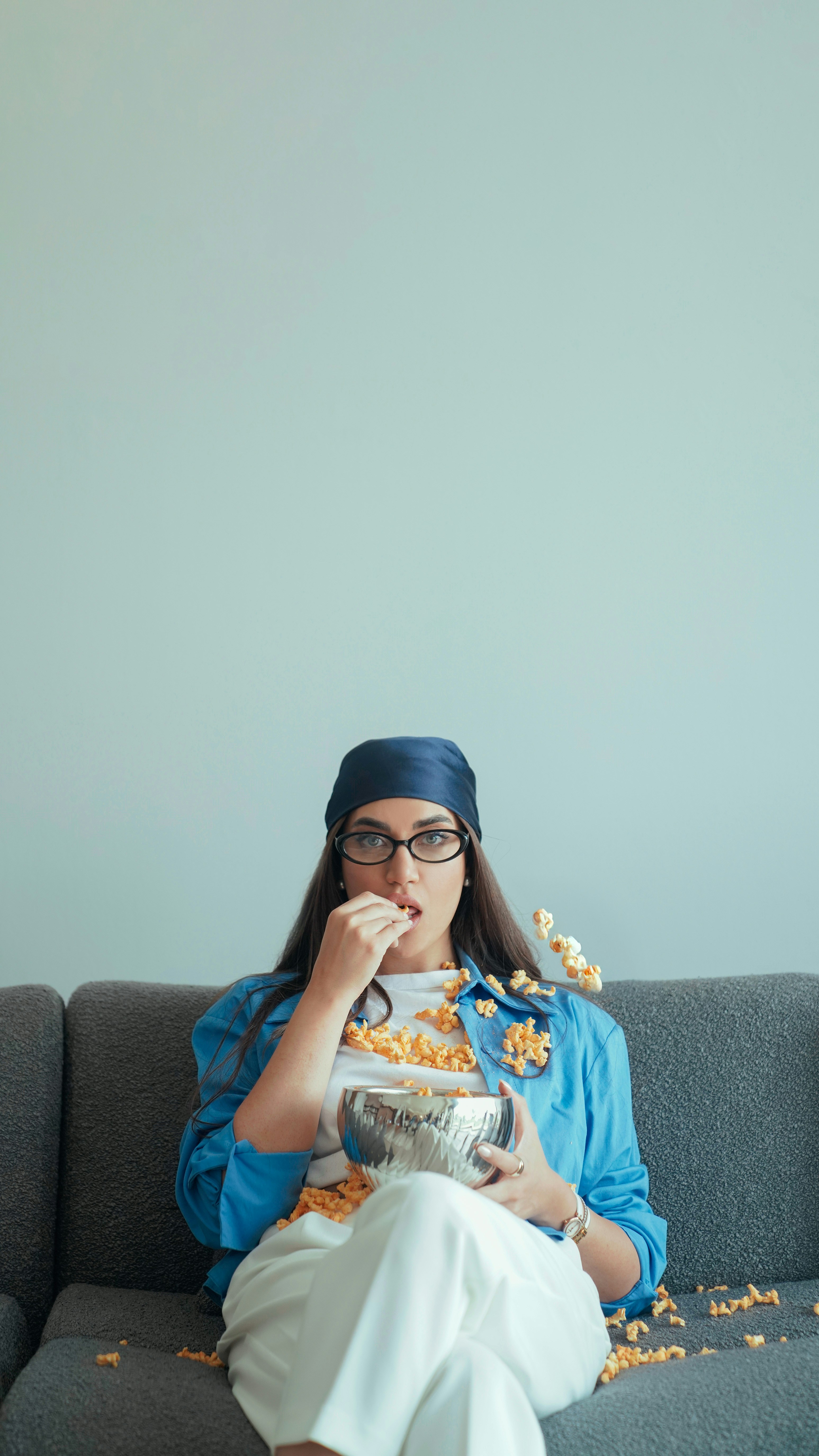Mulher bagunçada comendo pipoca no sofá.