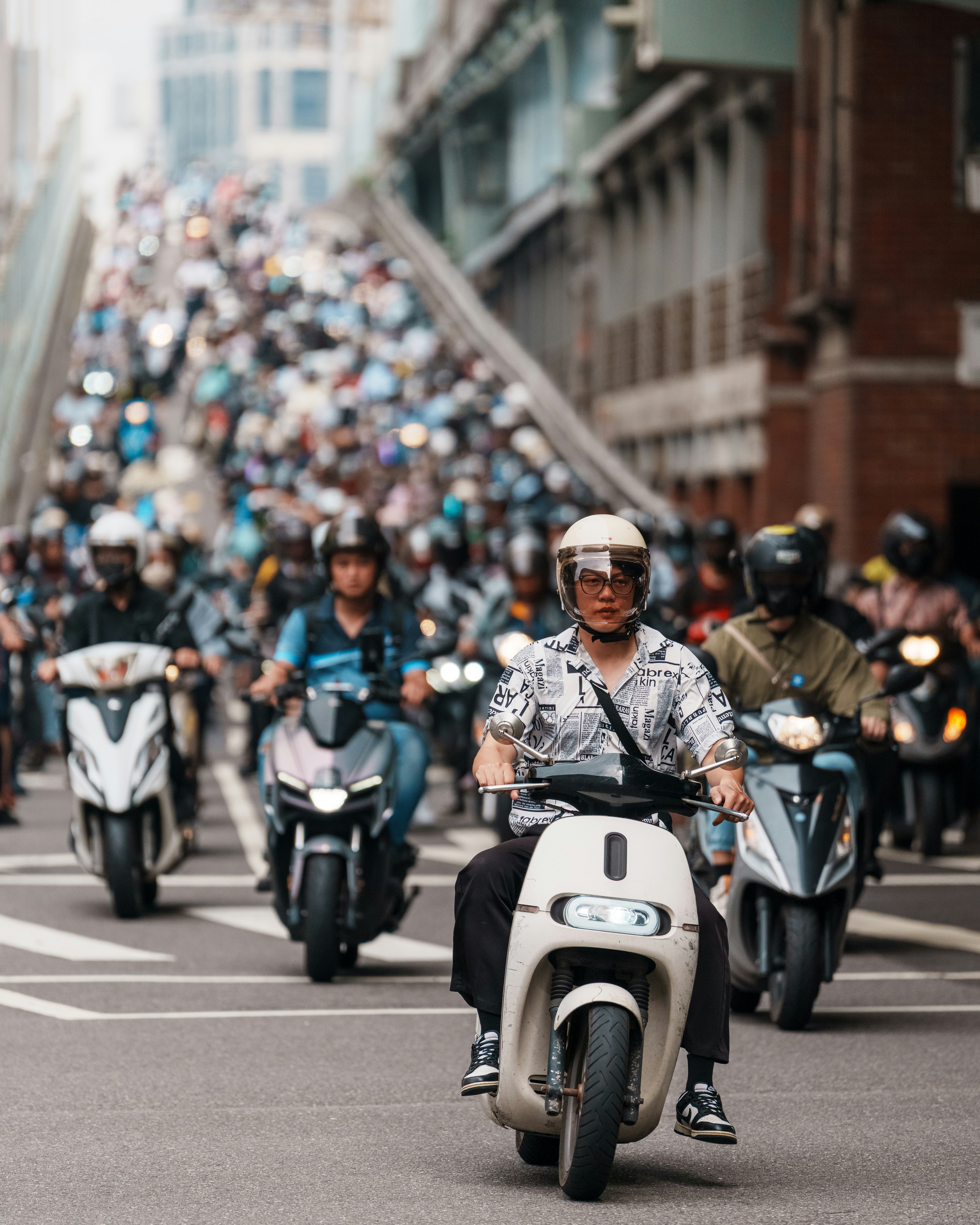 Many people riding scooters on a busy city street.
